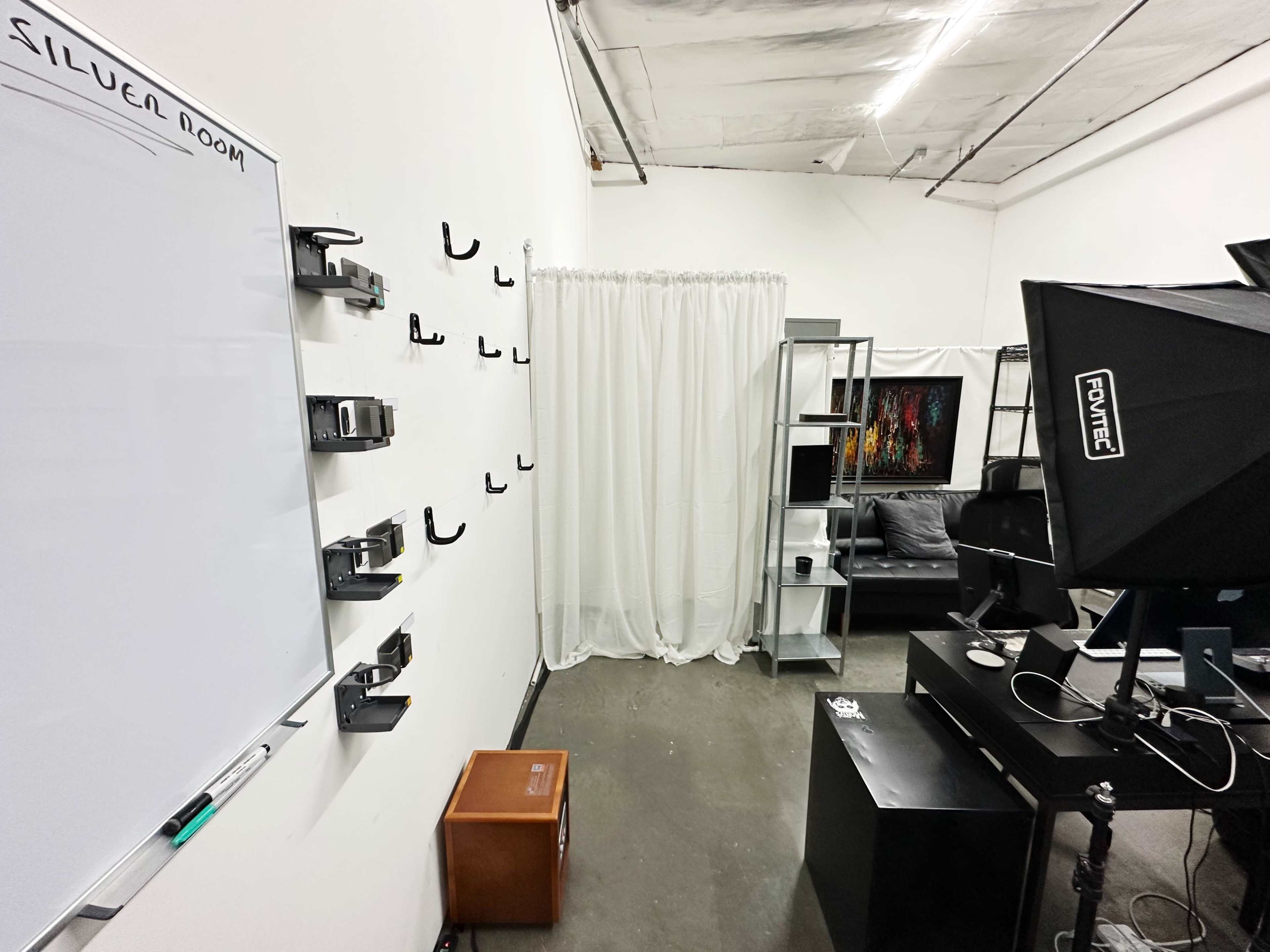 A minimalistic room features a whiteboard on one wall, a curtain separating areas, and various furniture pieces including a black desk and a couch.