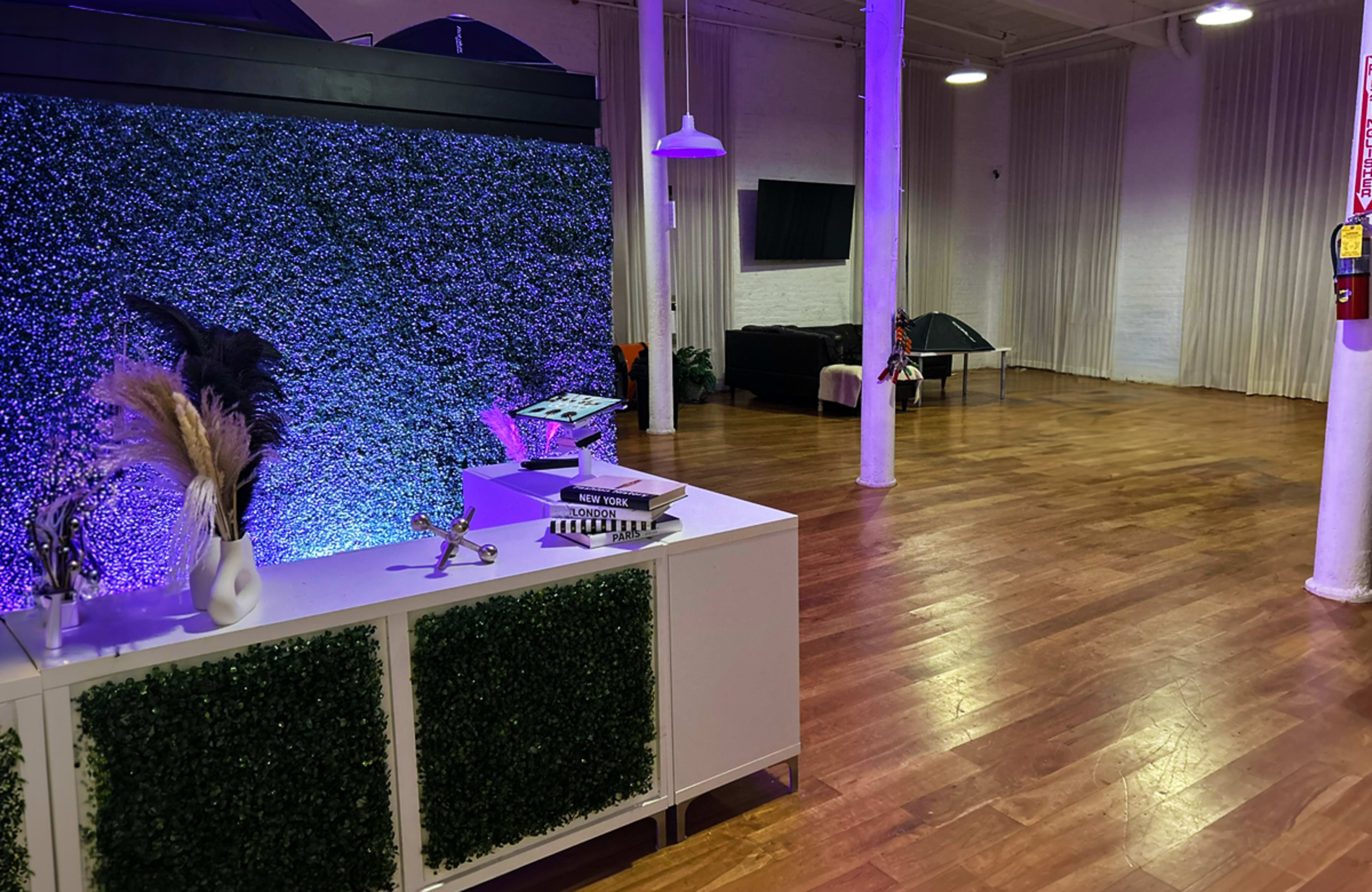 The image shows a spacious interior with hardwood floors, a green decorative wall, a reception area with a counter, and a seating area in the background.