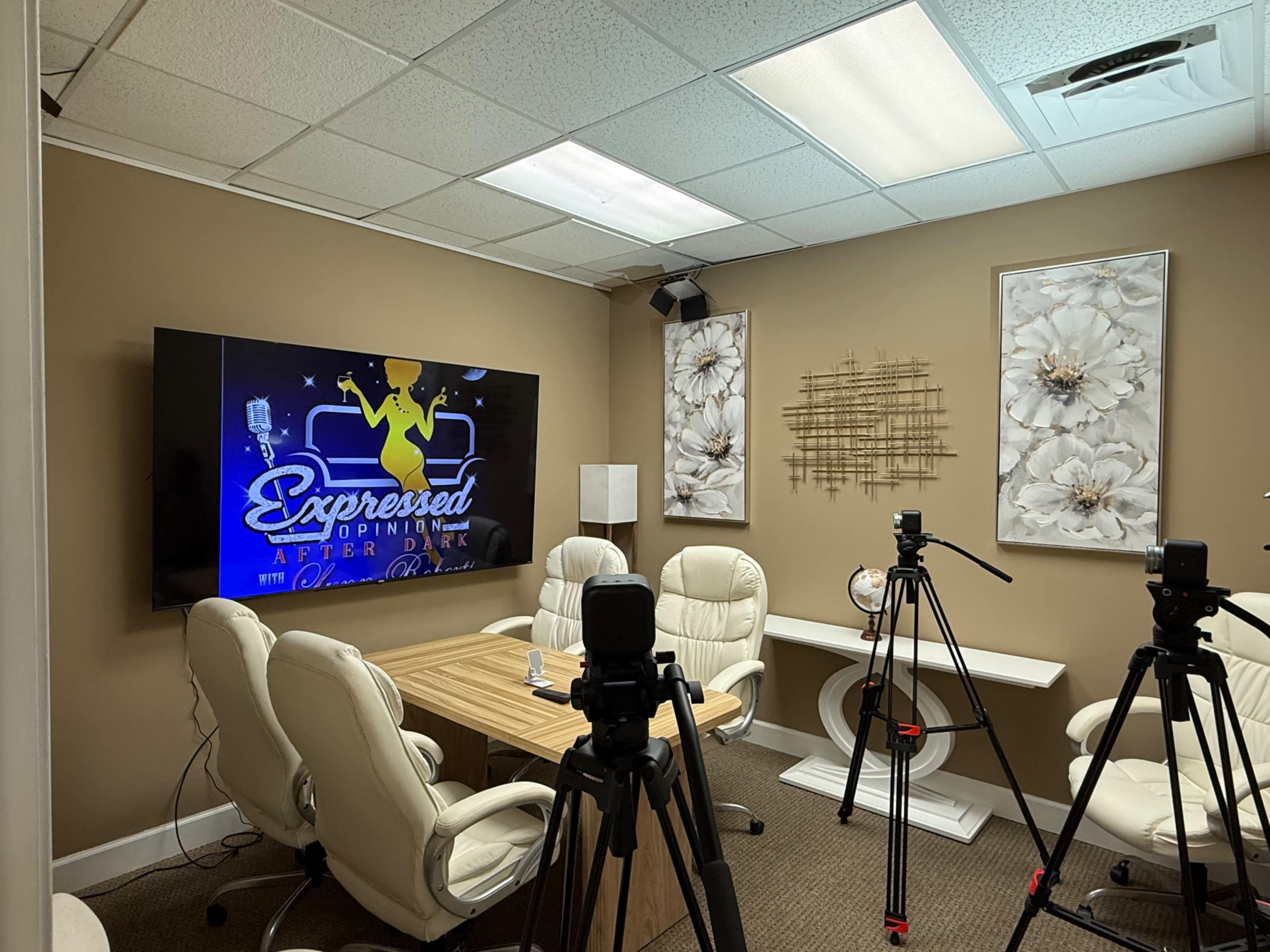 A conference room is set up with a large screen displaying the title "Expressed After Dark," surrounded by white chairs and filming equipment.