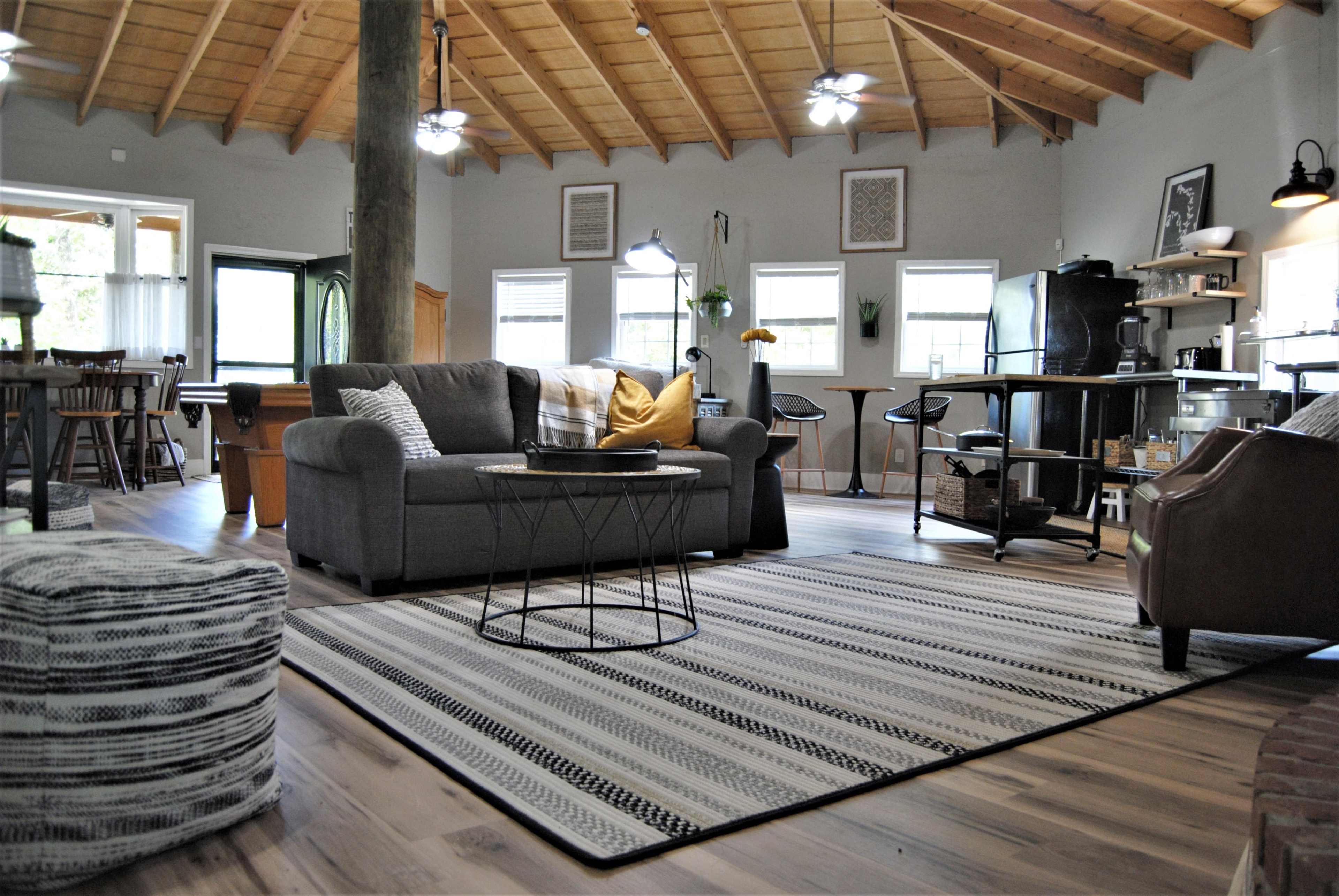 A modern, open-concept living area featuring a gray sofa, a circular coffee table, and a cozy rug, beneath a vaulted wooden ceiling.