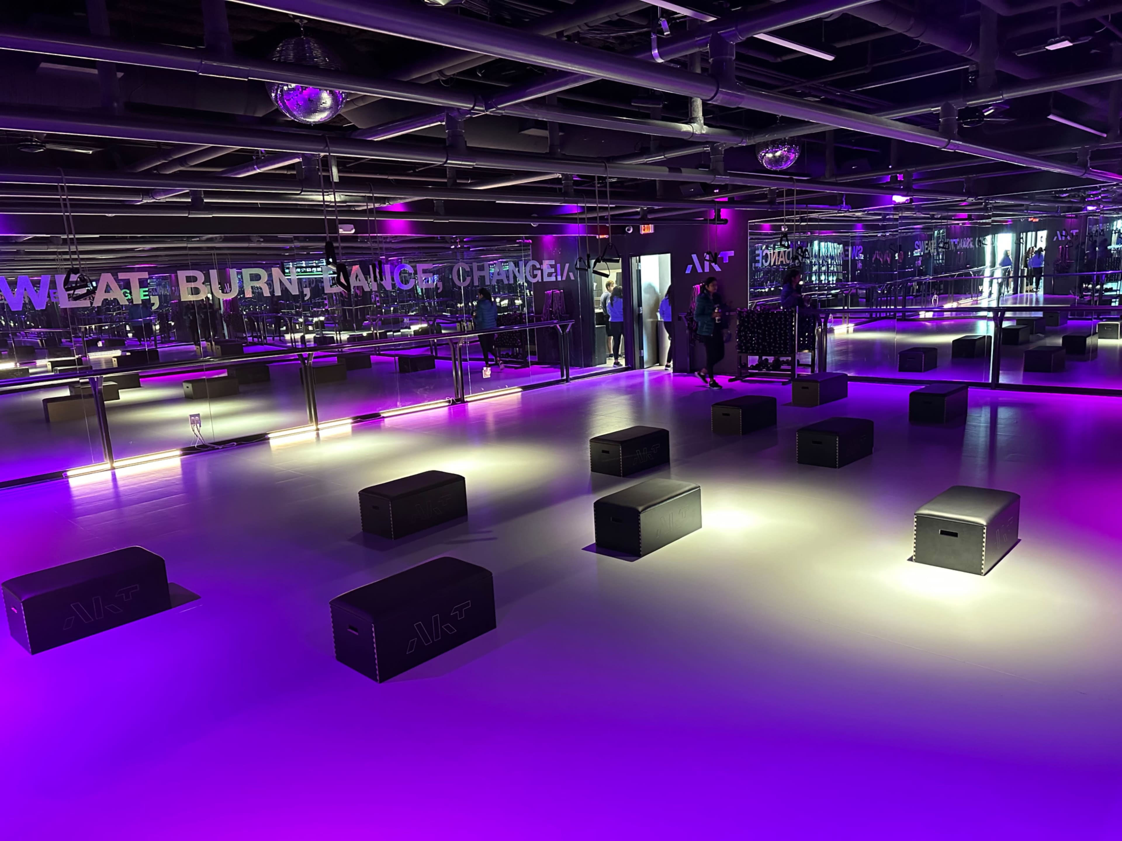 A modern fitness studio with a mirrored wall, purple lighting, and black exercise boxes arranged on the floor.