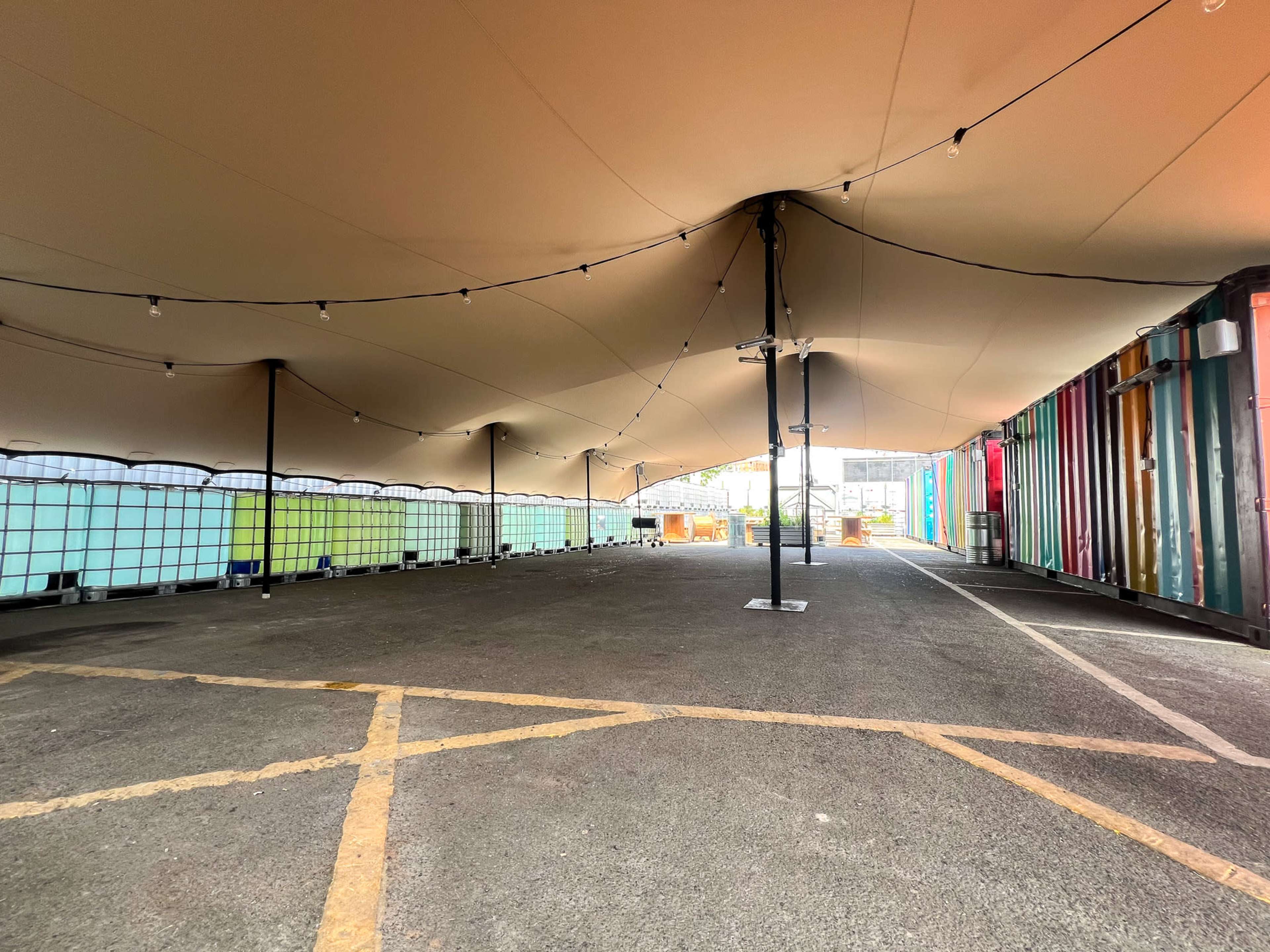 A spacious outdoor area covered by a large tent, with colorful shipping containers lining one side.