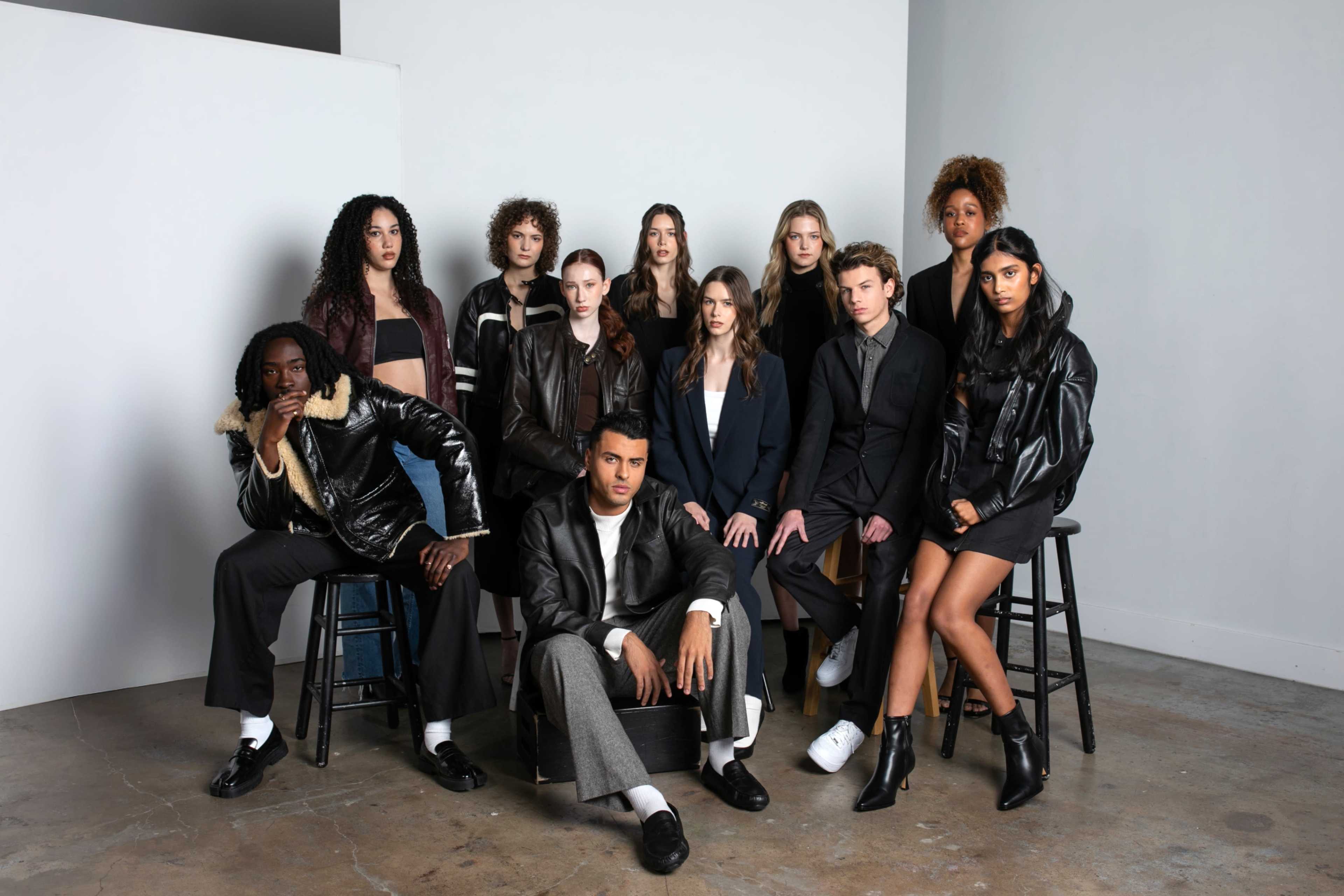 A group of twelve individuals poses for a photo in a studio setting, seated and standing on stools against a neutral backdrop.