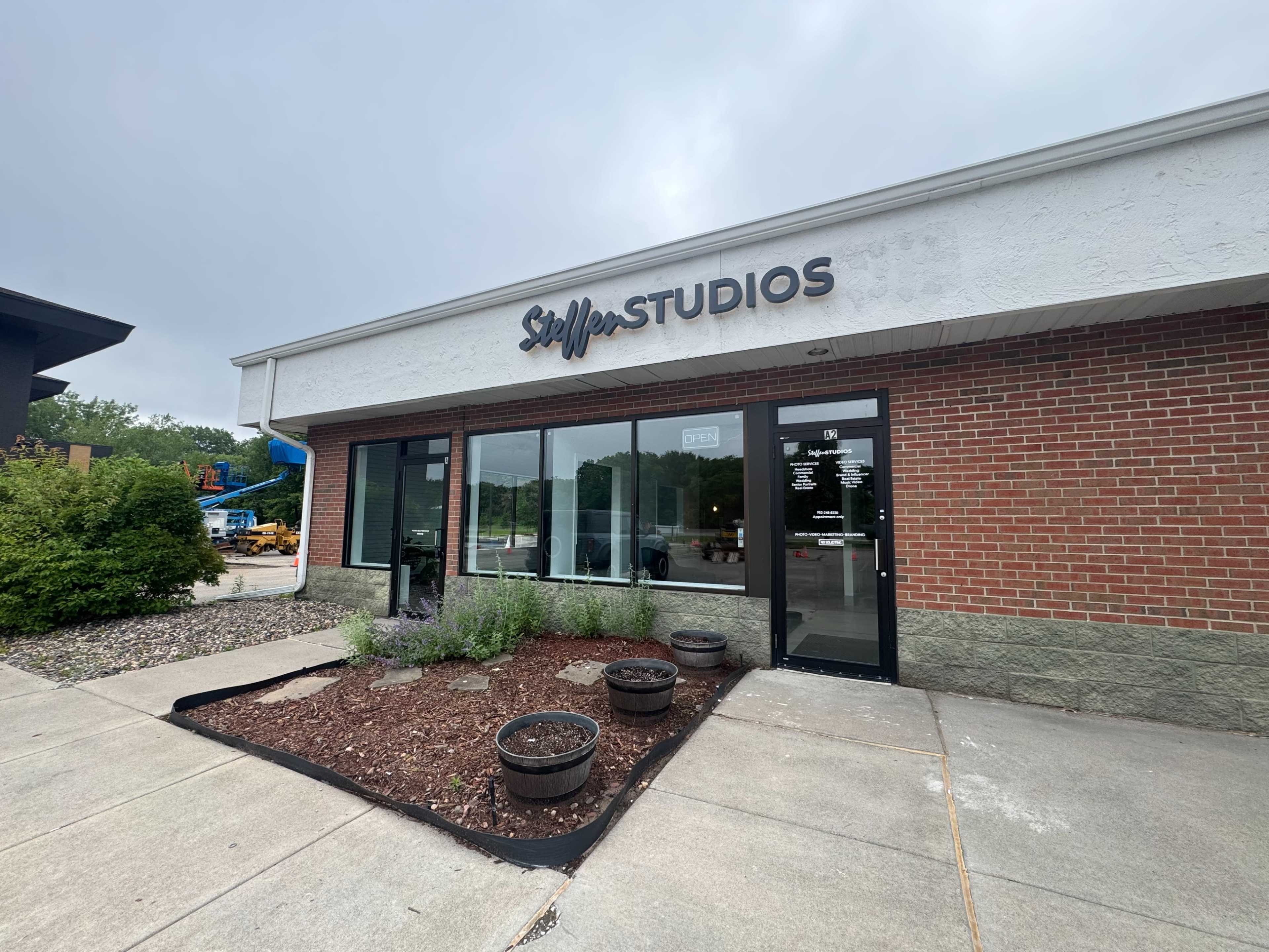 The image shows a building exterior with a sign that reads "Steffer Studios," featuring a landscaped area in front with planters.