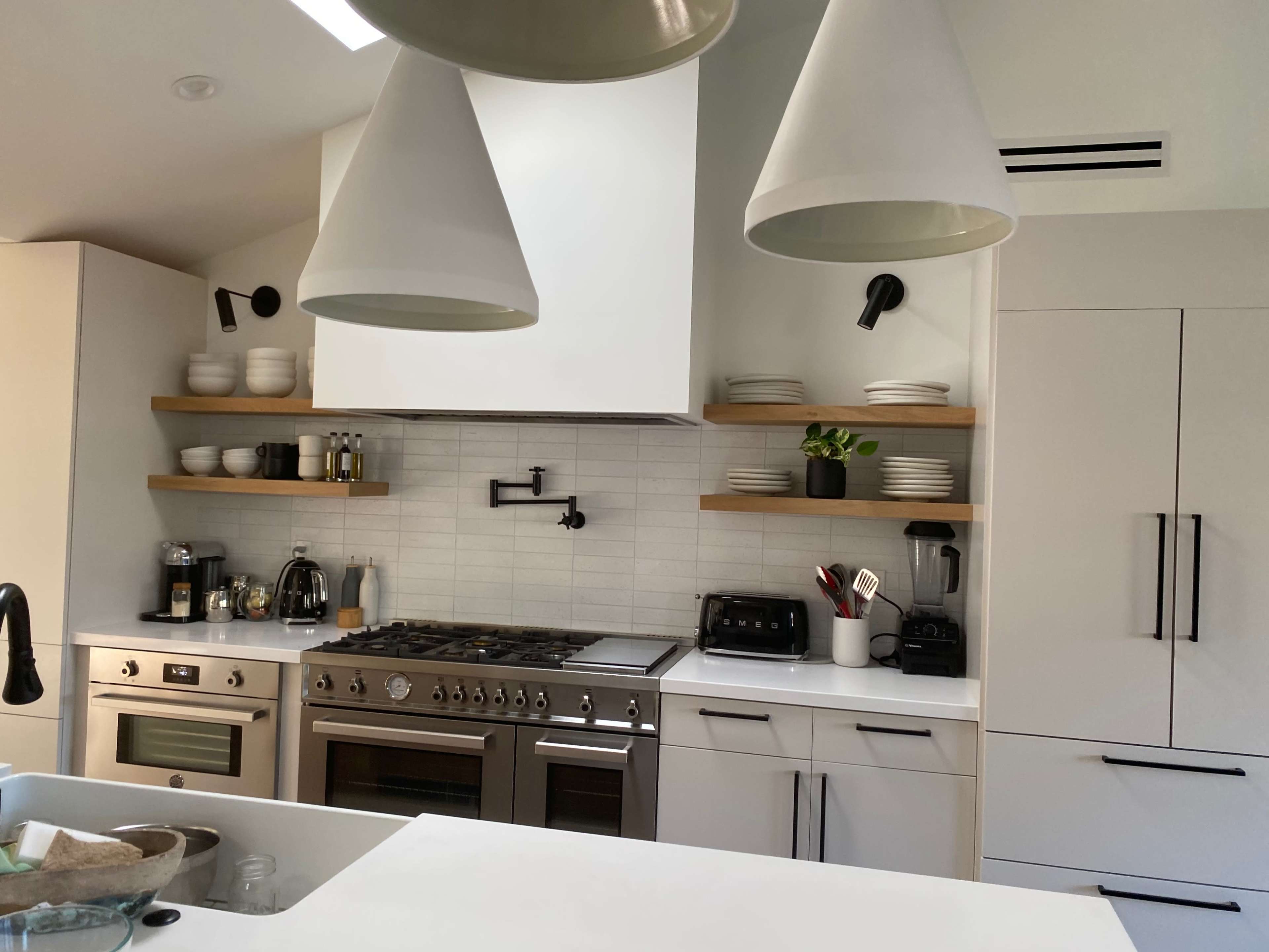 The image shows a modern kitchen with stainless steel appliances, open shelving with dishware, and a large gas stove.