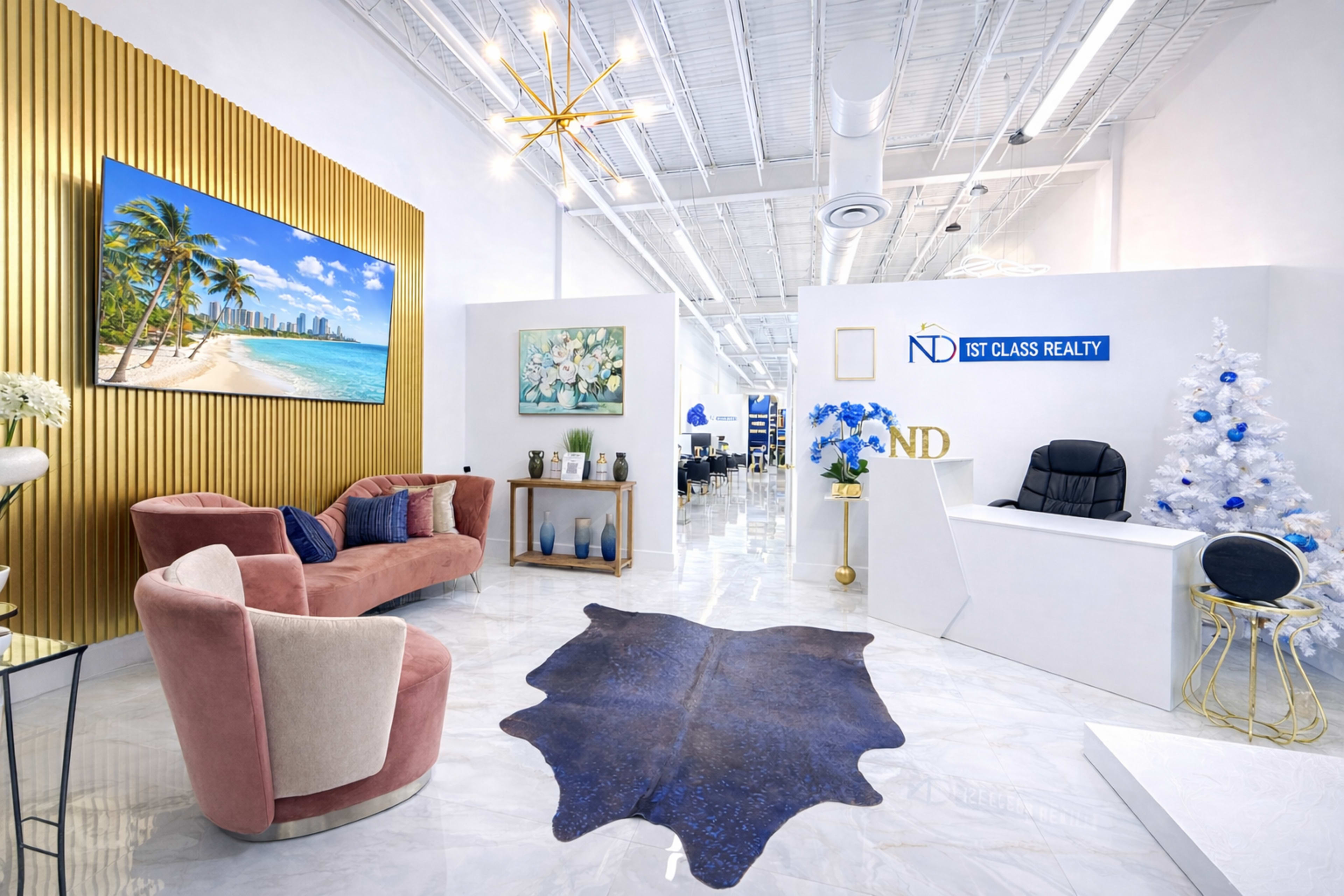 The image shows a modern office reception area with a seating arrangement, a large wall-mounted screen displaying a beach scene, and a decorated Christmas tree.