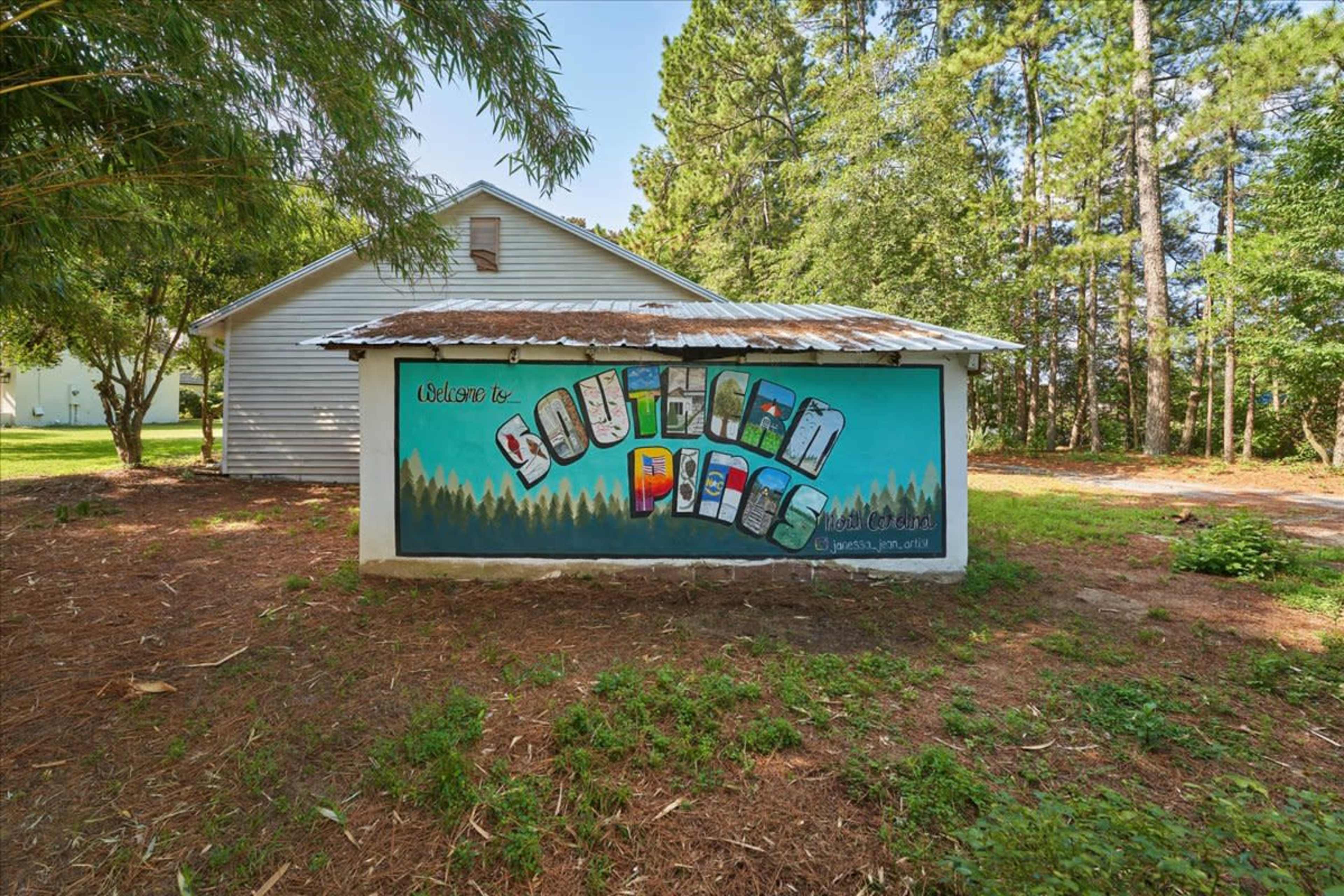 A mural on a wall that reads "Welcome to Southern Pines," set against a backdrop of trees and a nearby white building.