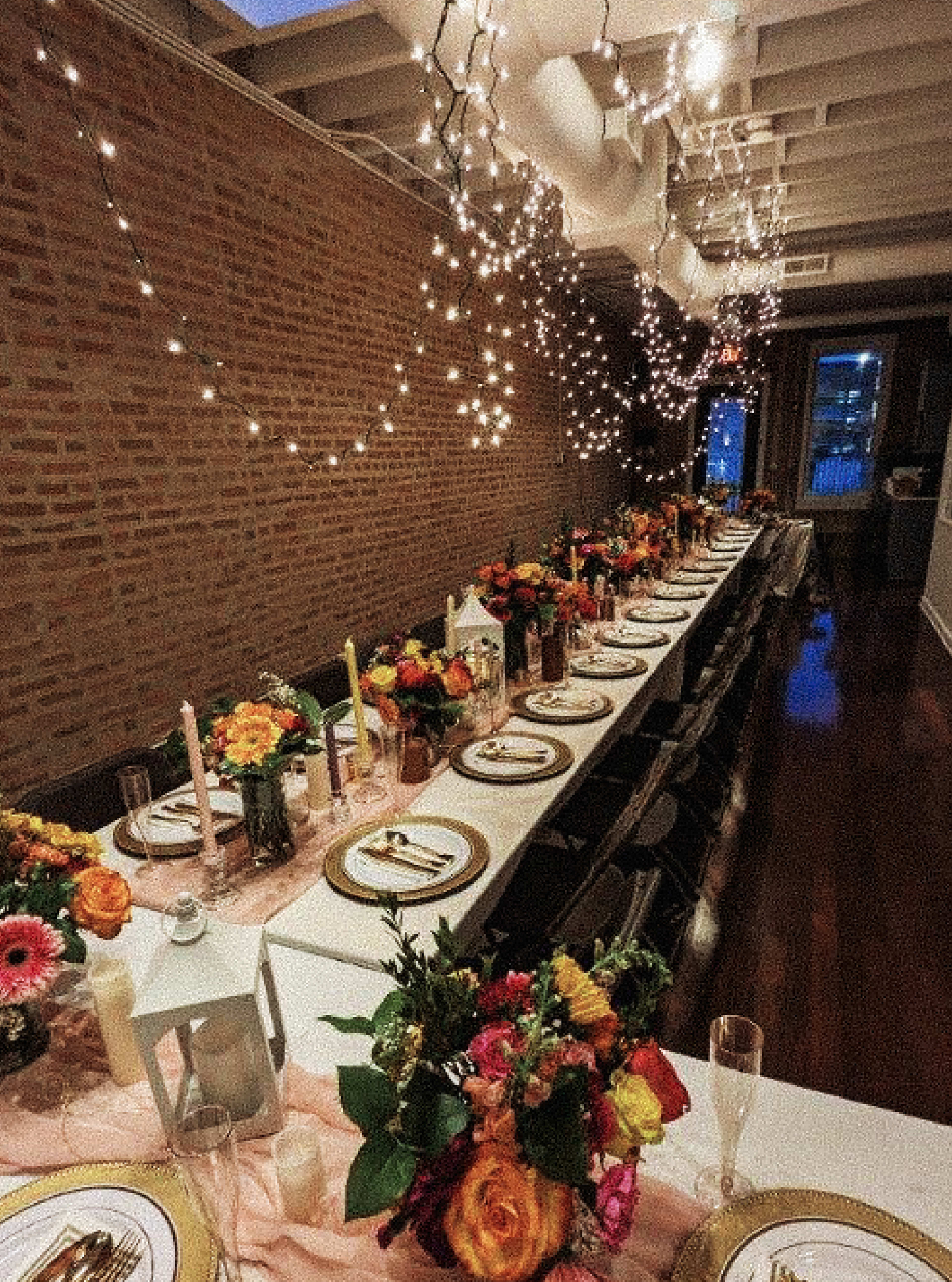 A long banquet table is elegantly set with floral centerpieces and surrounded by chairs in a warmly lit indoor venue.