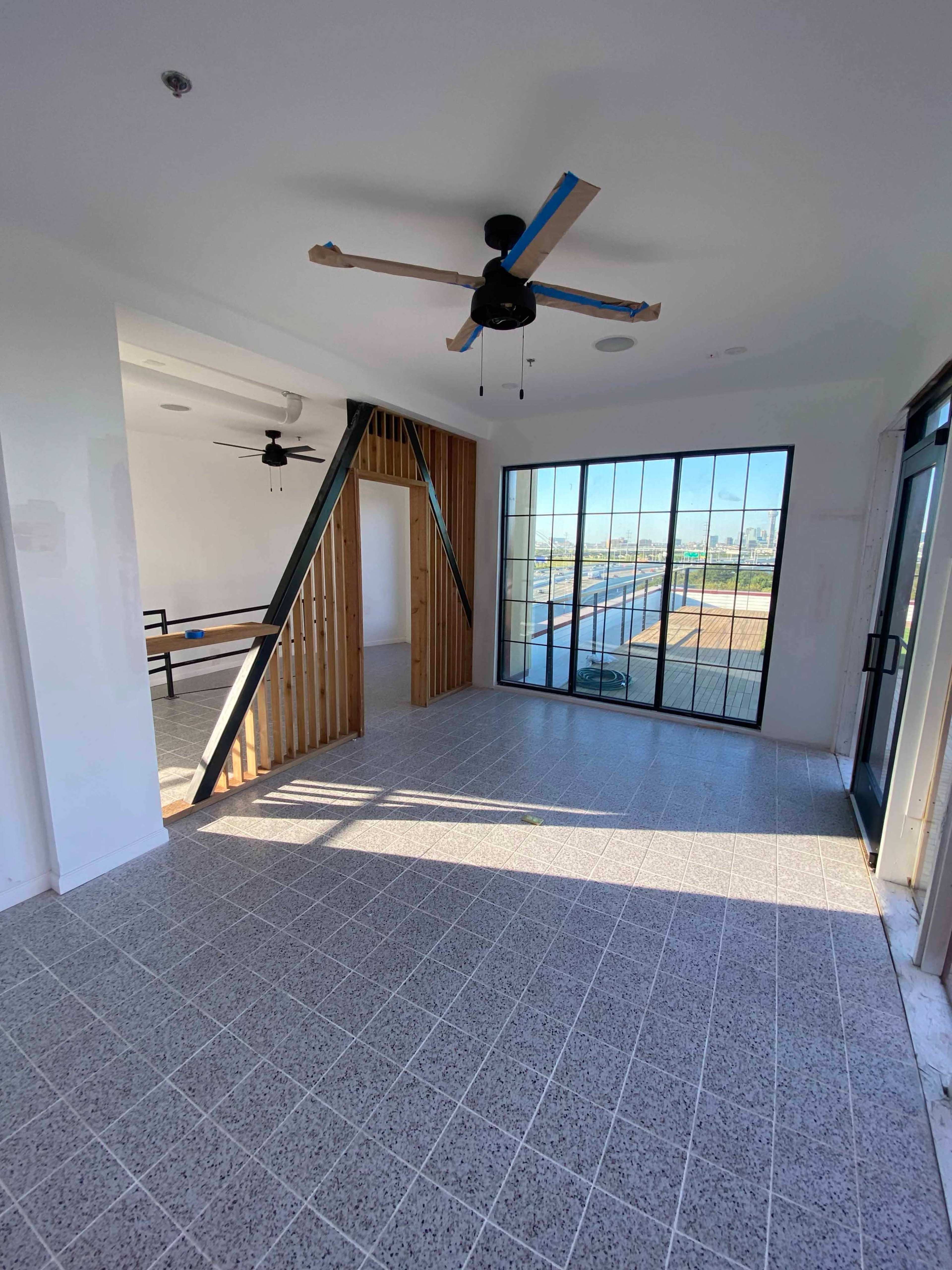 A spacious interior room featuring large windows, a ceiling fan, and a mix of wooden and tiled flooring.