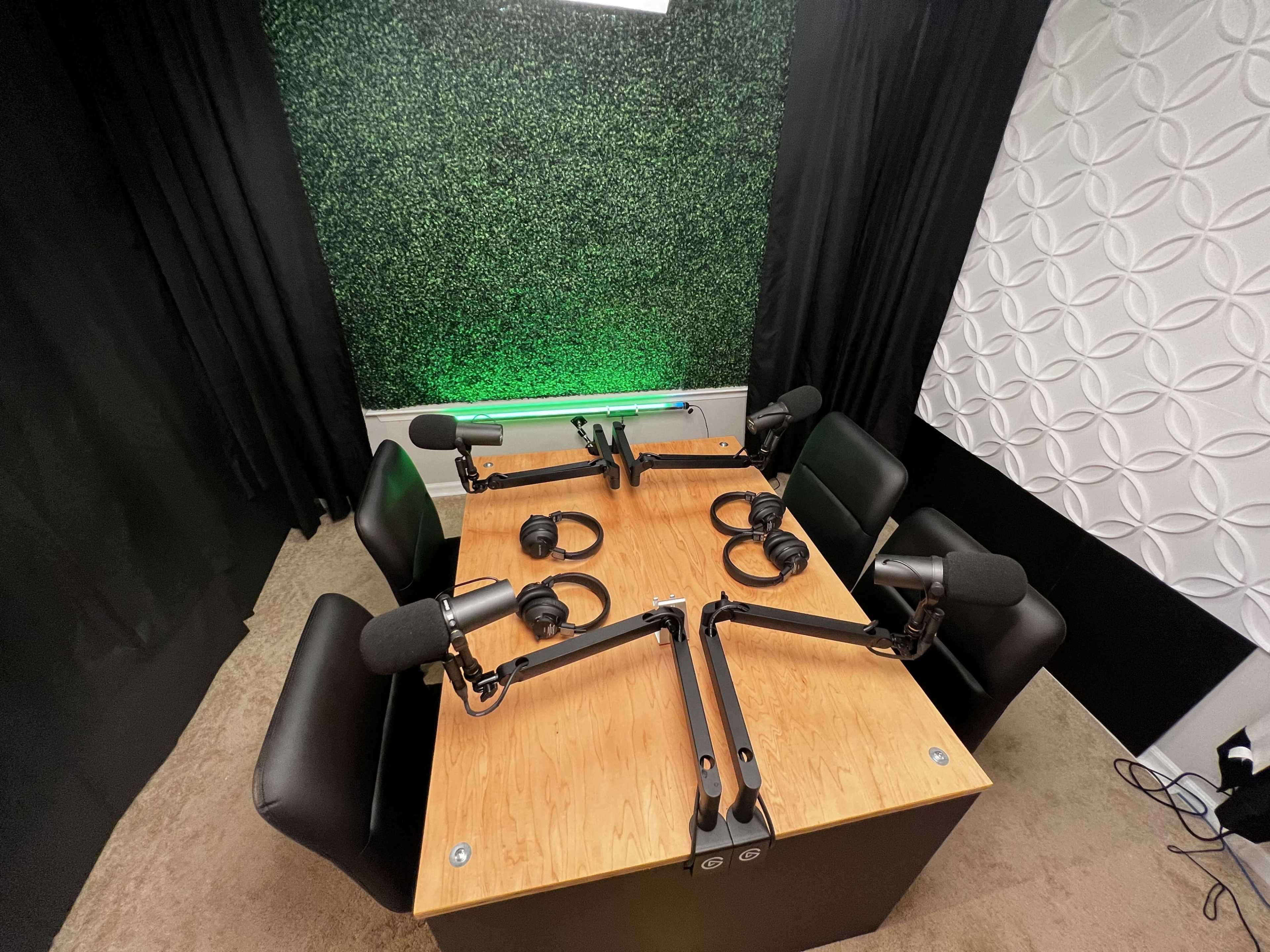 A podcast studio featuring a wooden table with four chairs, two microphone arms, and headphones arranged for recording.