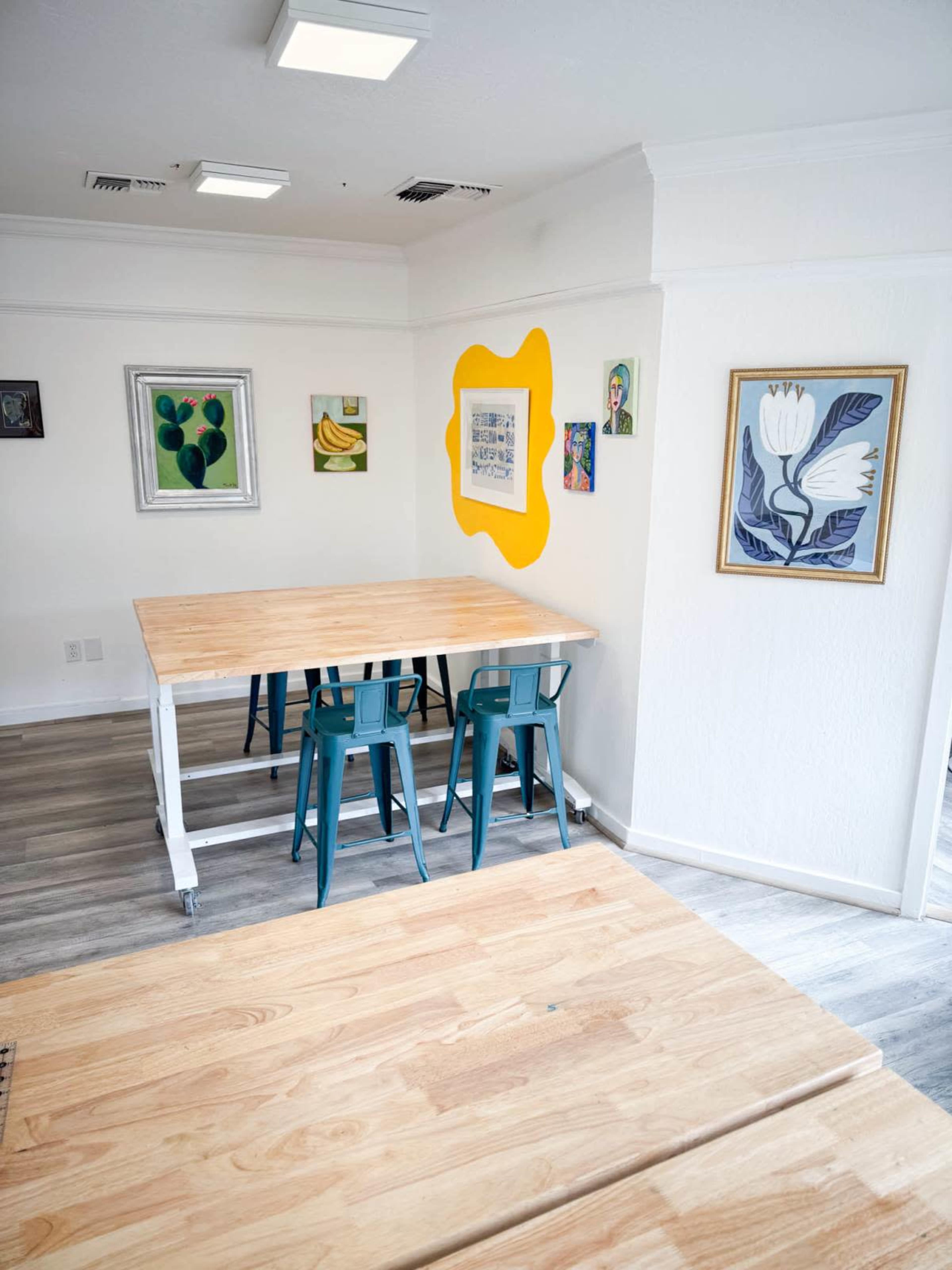 A bright room features a wooden table with teal chairs and colorful artwork on the walls.