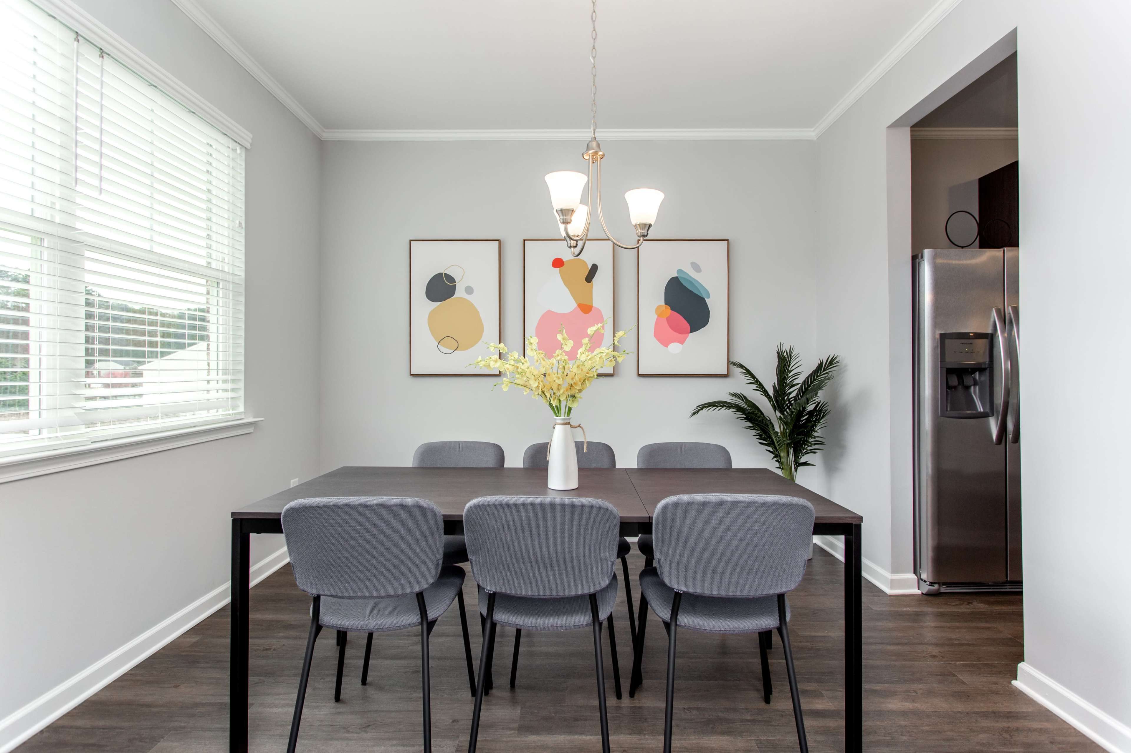 A modern dining room features a black table surrounded by six gray chairs, with a vase of flowers on the table and abstract artwork on the walls.
