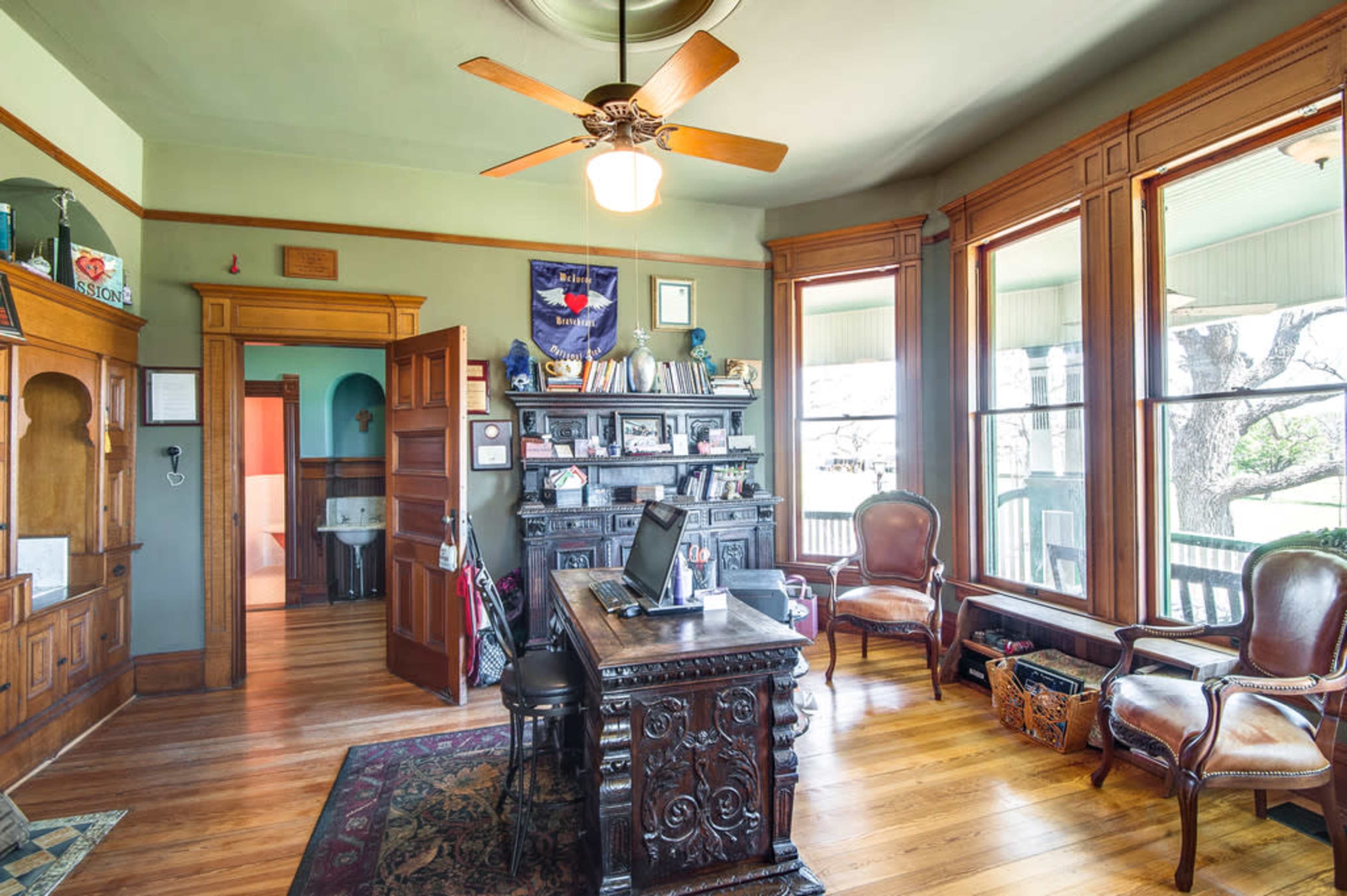 A well-furnished room with a large wooden desk, two upholstered chairs, and windows that let in natural light.