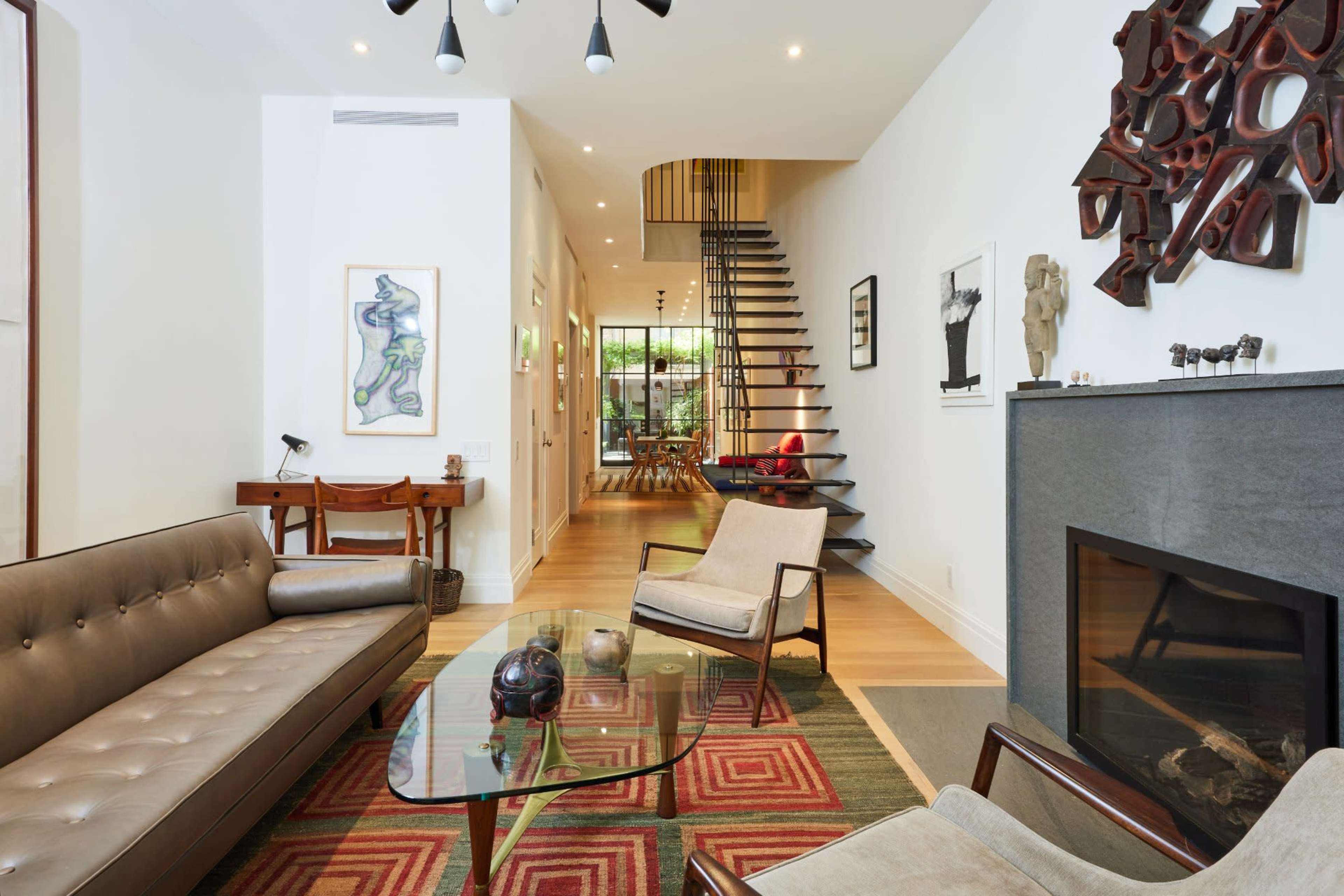The image depicts a modern living room with a leather sofa, glass coffee table, and a staircase leading to an upper level.