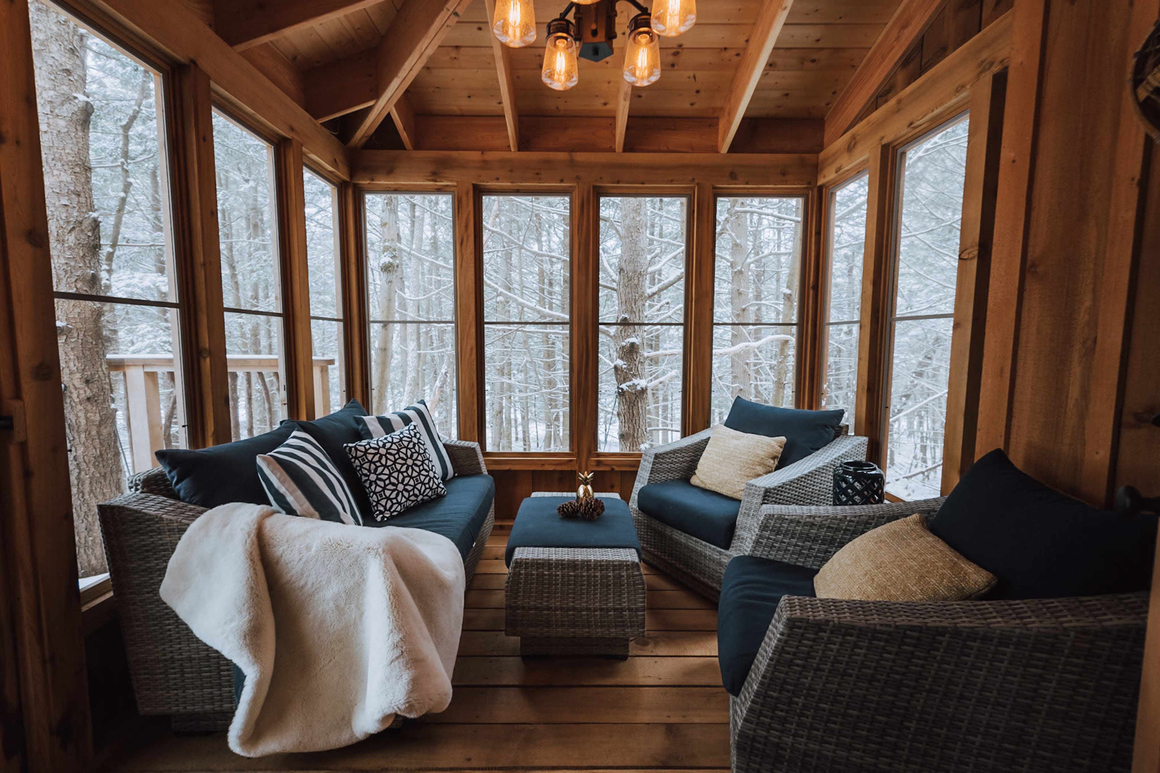 A cozy indoor seating area with wicker furniture and large windows overlooking a snowy forest.