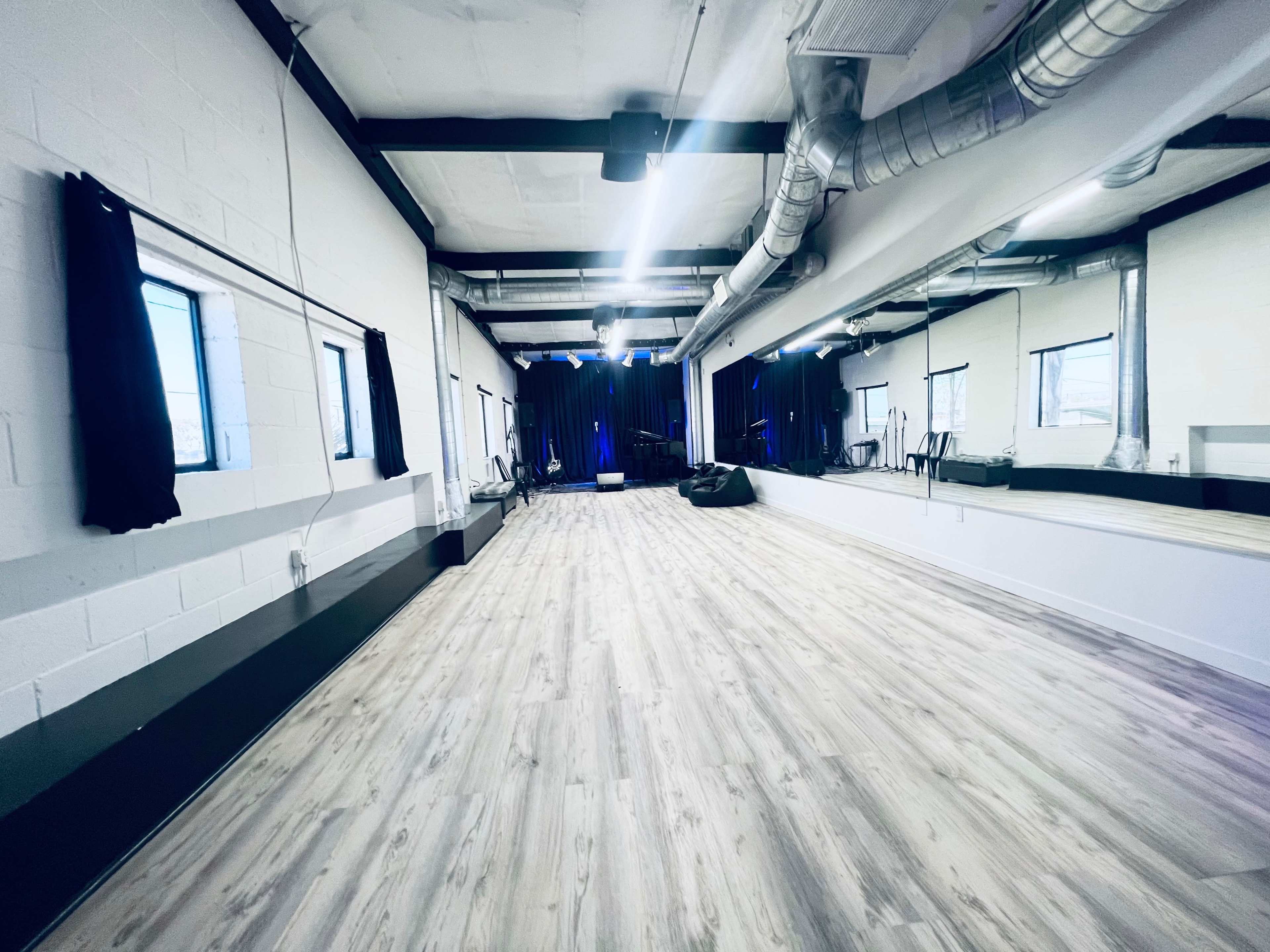 A spacious dance studio with wooden flooring, large mirrors, and a dark curtain backdrop.