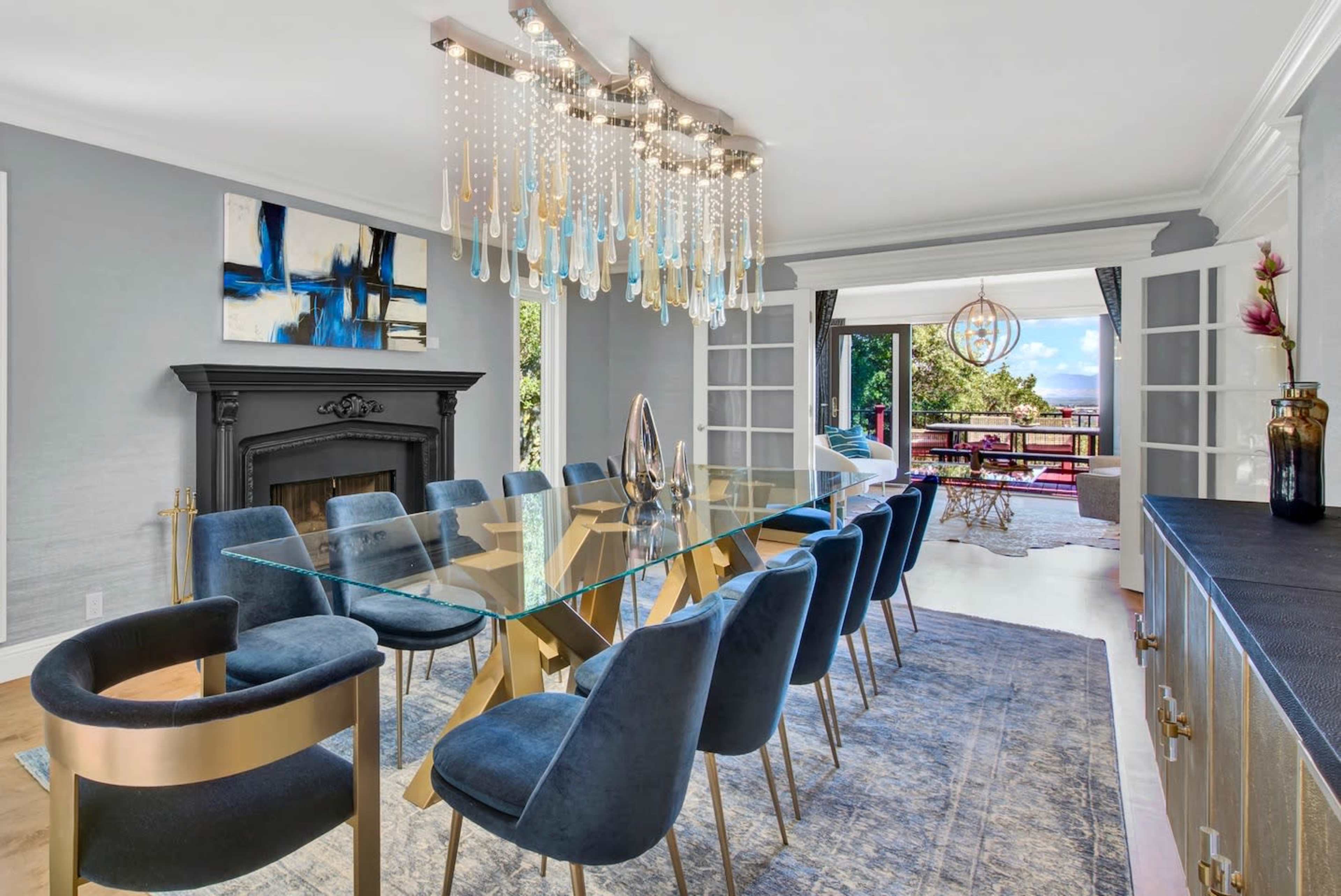 A modern dining room features a glass table surrounded by eight navy blue chairs and a decorative chandelier above.