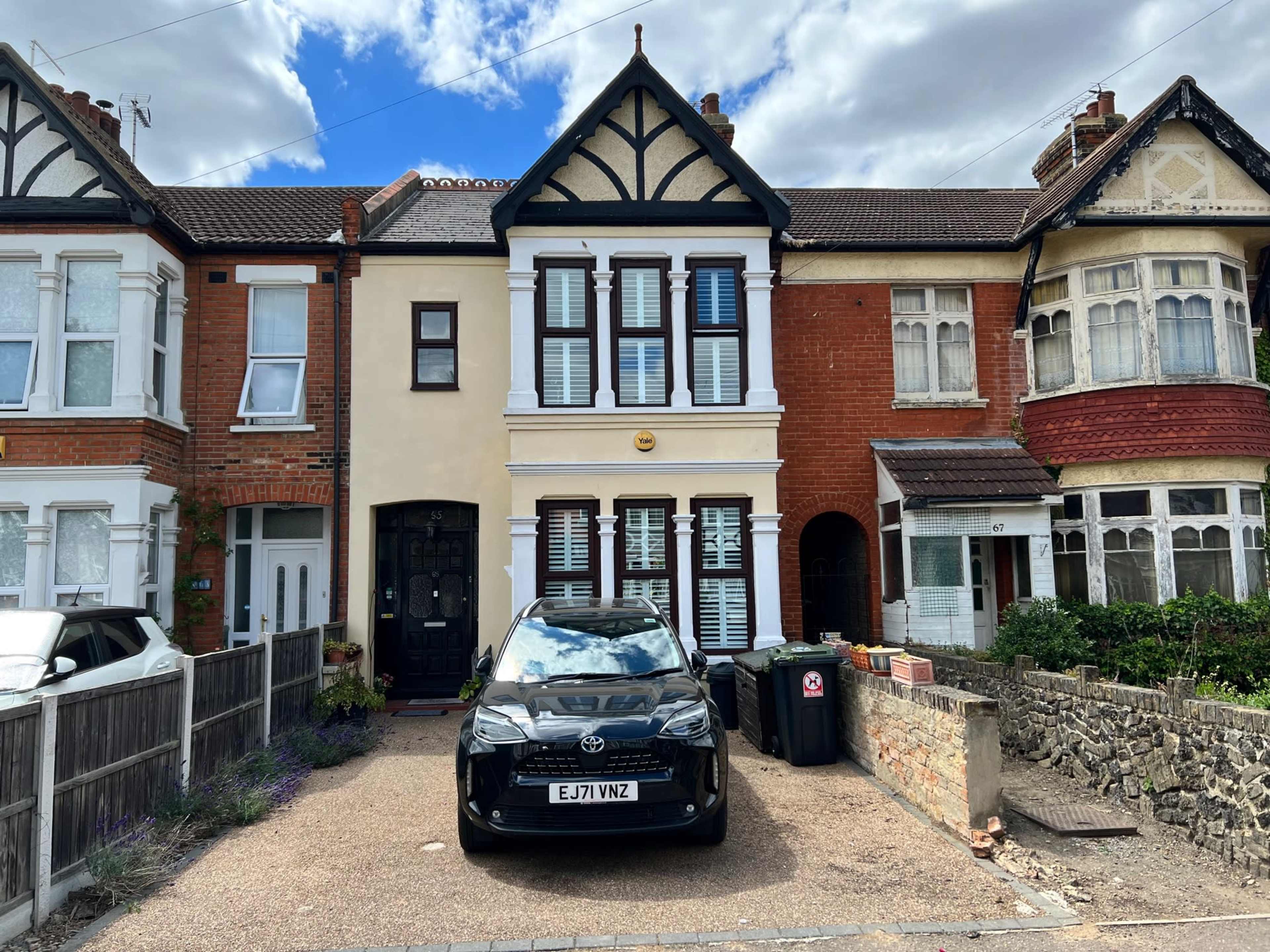 A black car is parked in front of a row of three houses, featuring a mix of architectural styles.