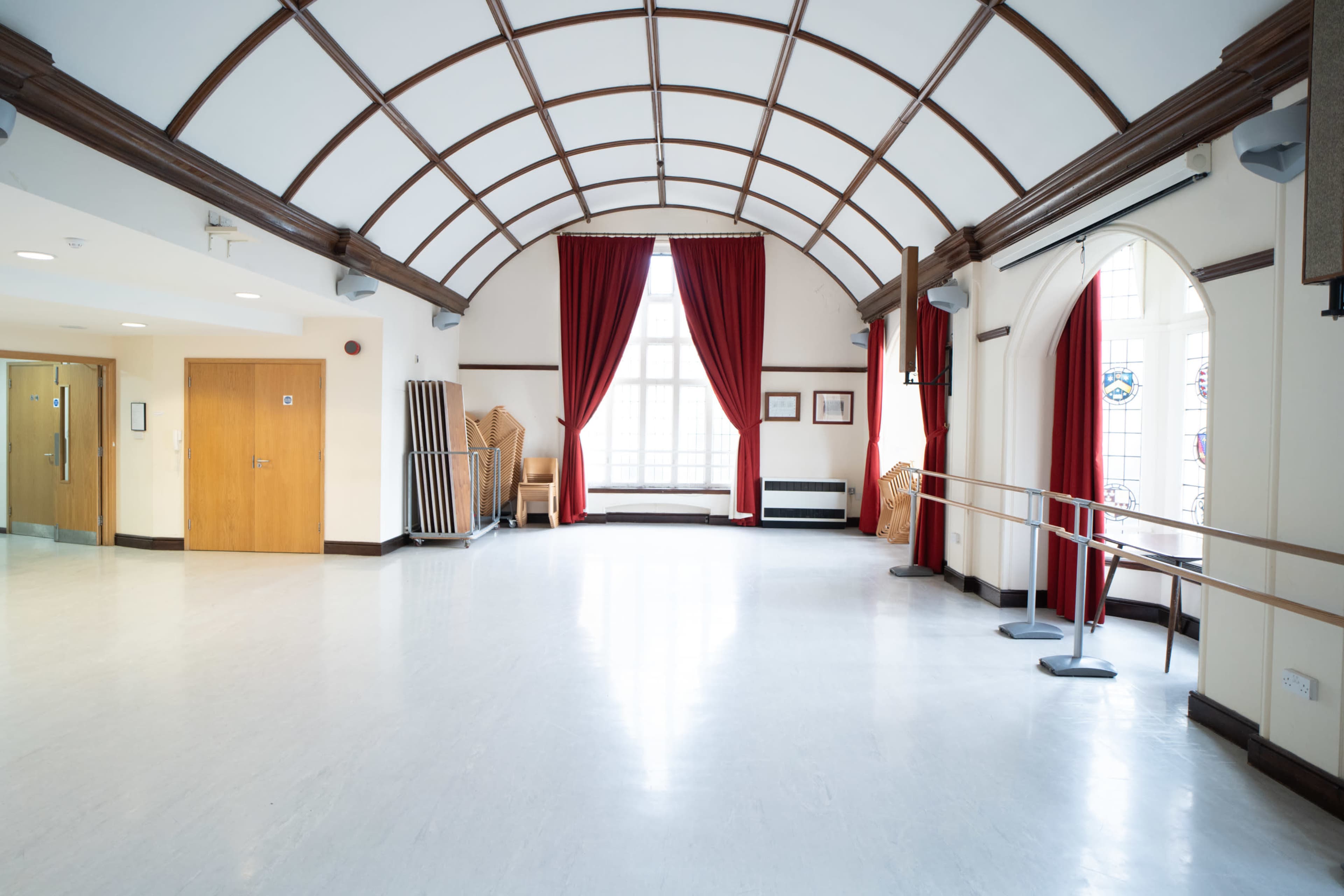 The image shows a spacious hall with a high arched ceiling, wooden accents, red curtains, and a ballet barre along one wall.