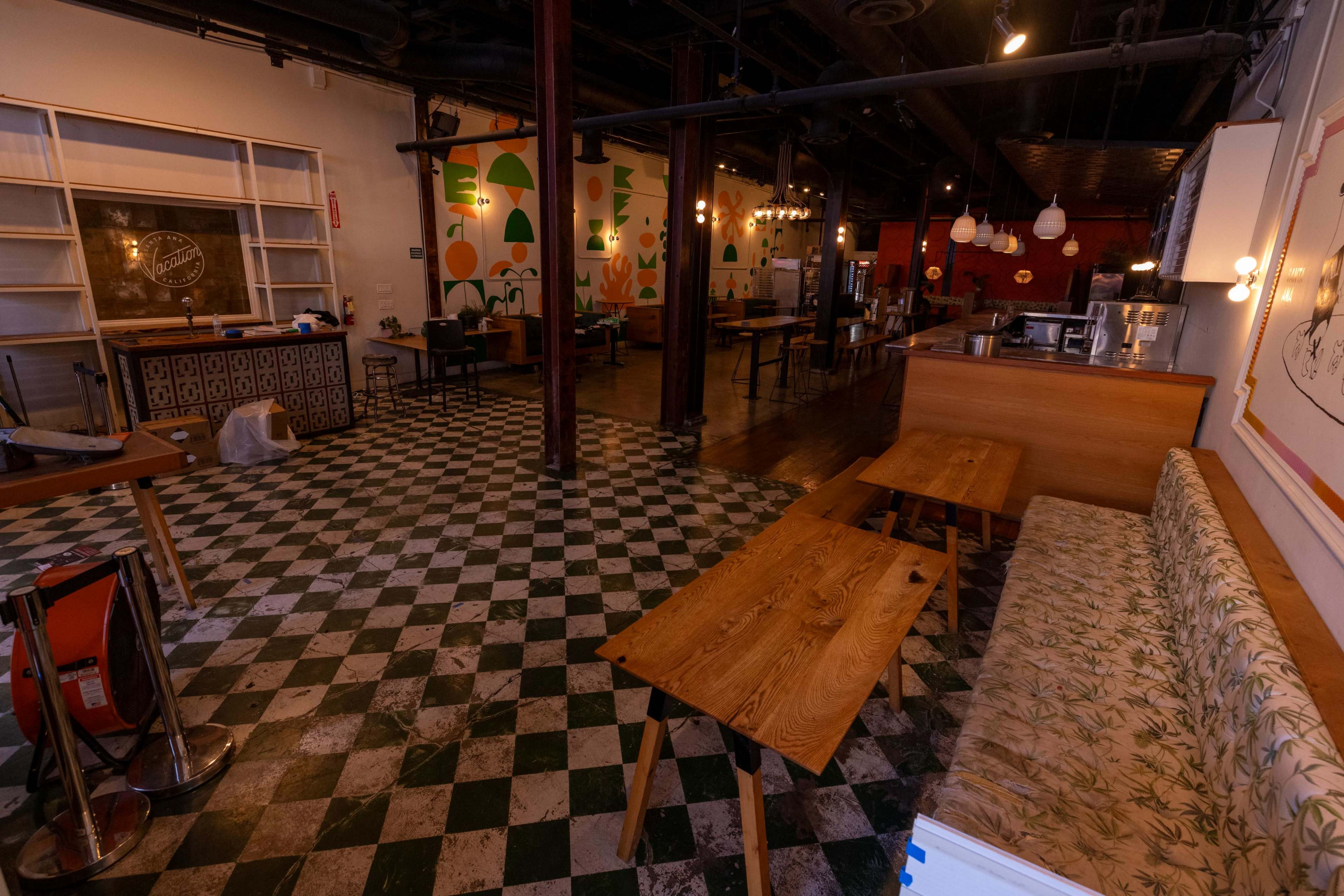 The image shows the interior of a restaurant with a checkered floor, wooden tables, and colorful wall murals.