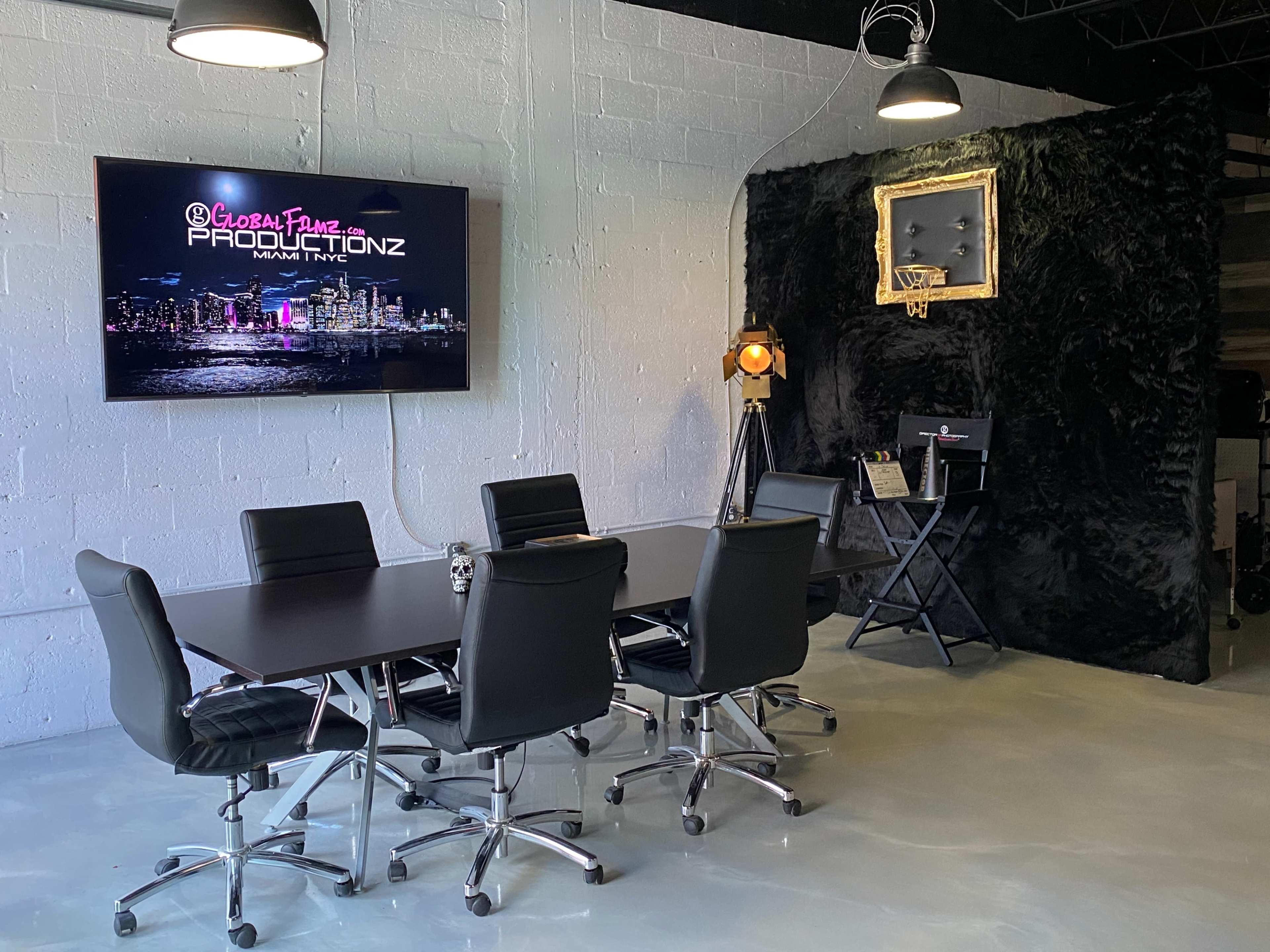 A conference room with a black table and six chairs is shown, featuring a large TV displaying "Global Plane Productionz" and a wall with a basketball hoop and spotlight.