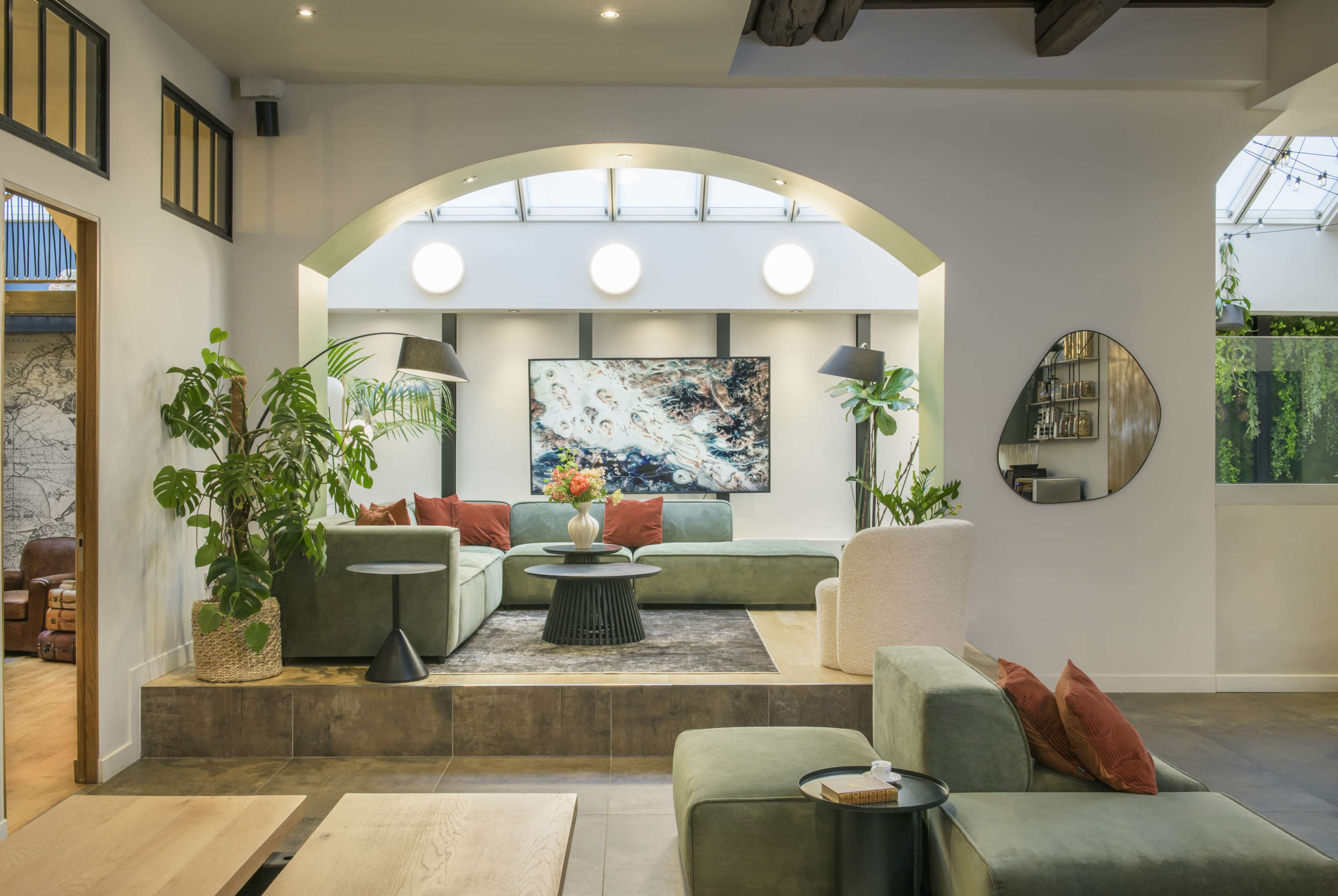 The image shows a modern interior living space featuring a green sectional sofa, decorative plants, and an abstract art piece on the wall.