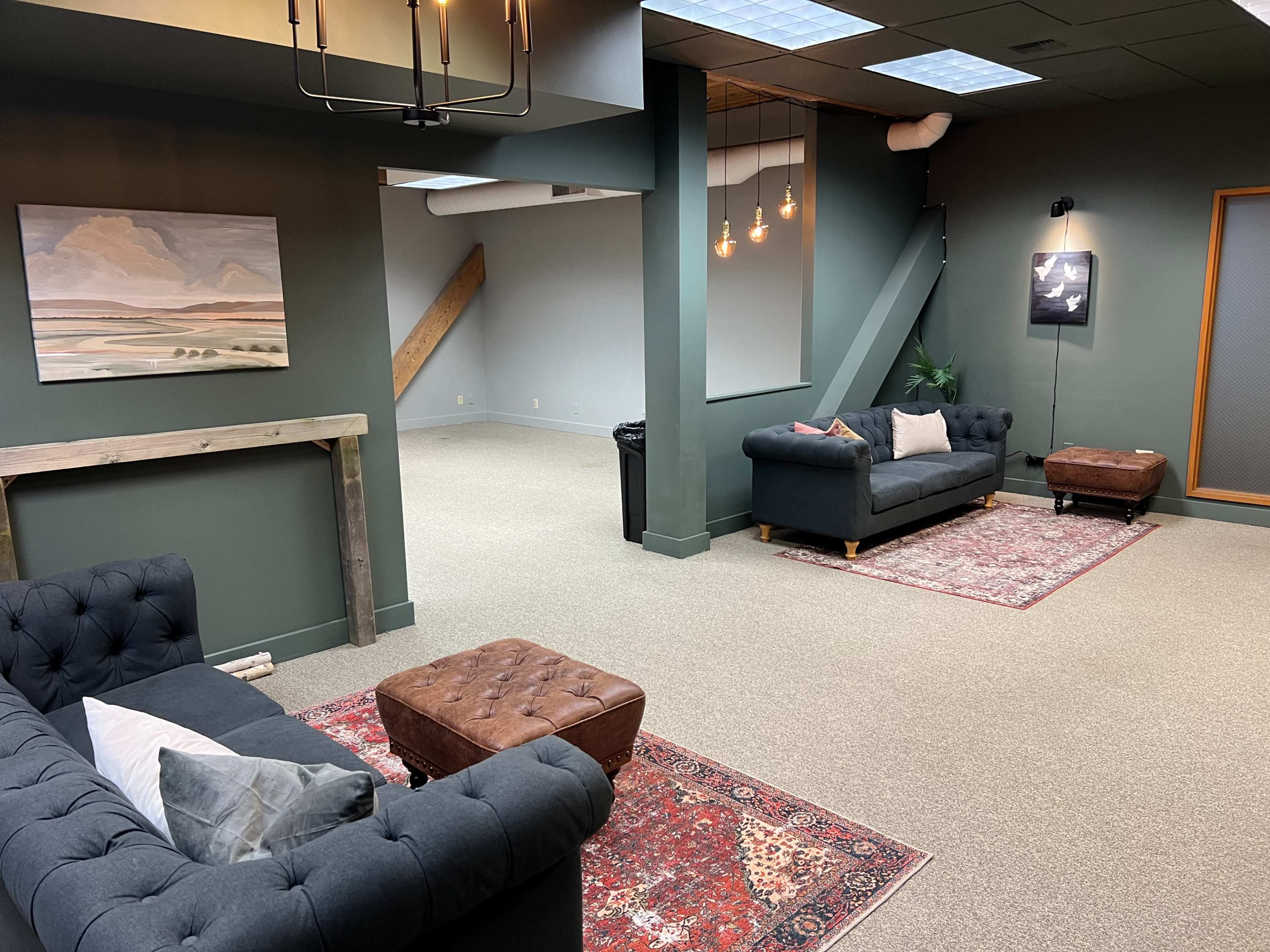 A spacious, modern room with two dark sofas, a coffee table, and an area rug, complemented by a painting on the wall and pendant lights overhead.