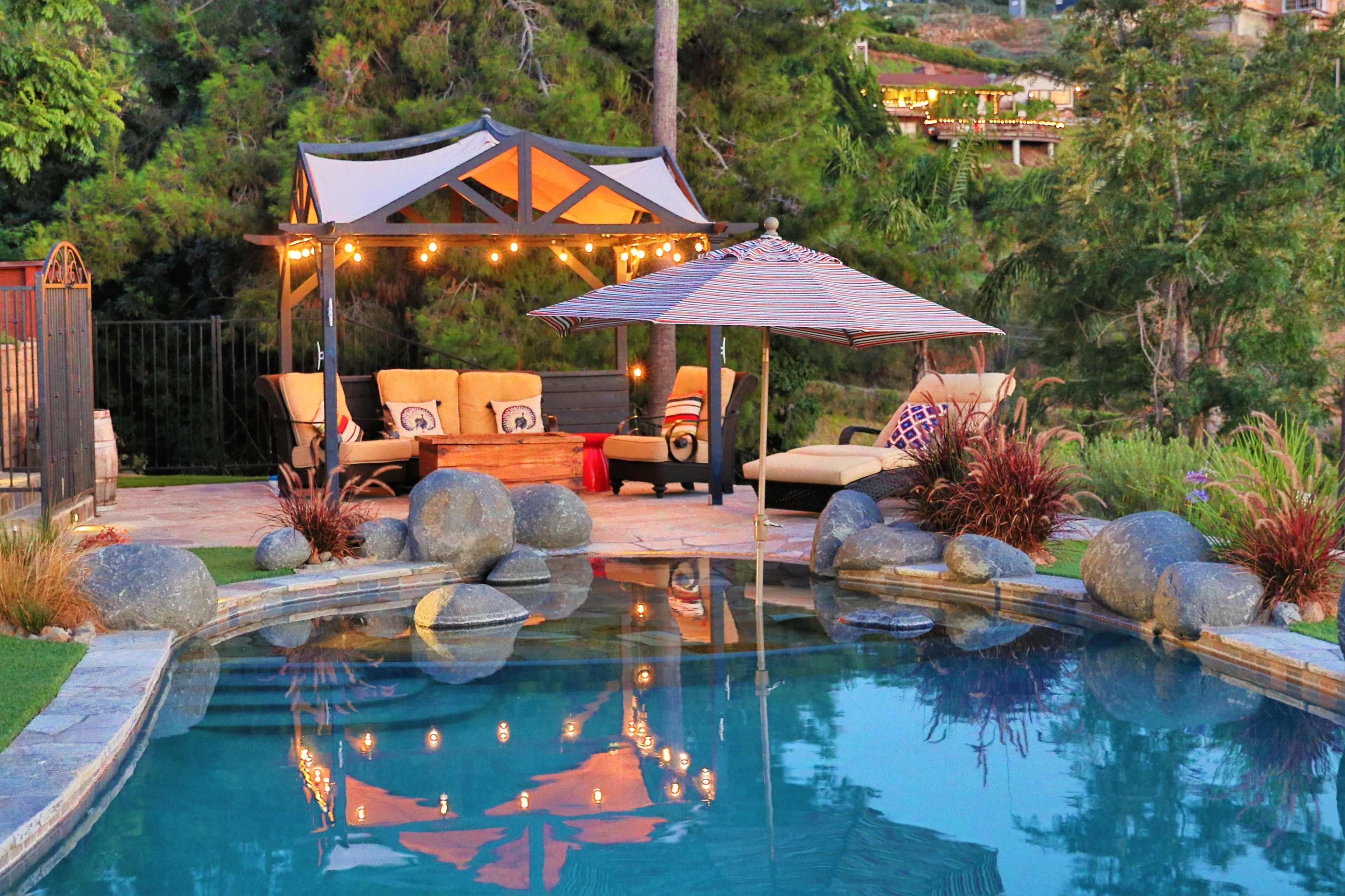 The scene features a landscaped backyard with a pool reflecting lounge furniture and a gazebo adorned with lanterns.