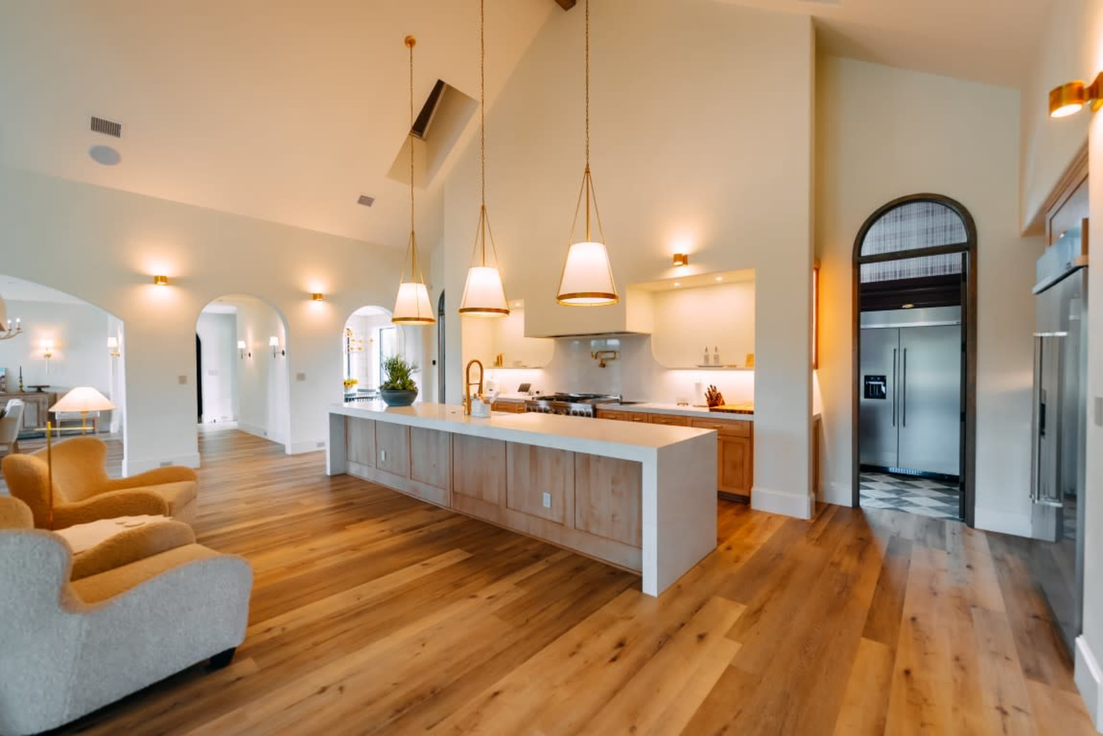 The image shows a modern kitchen with an island, two pendant lights, and large windows, featuring wood flooring and an open layout.