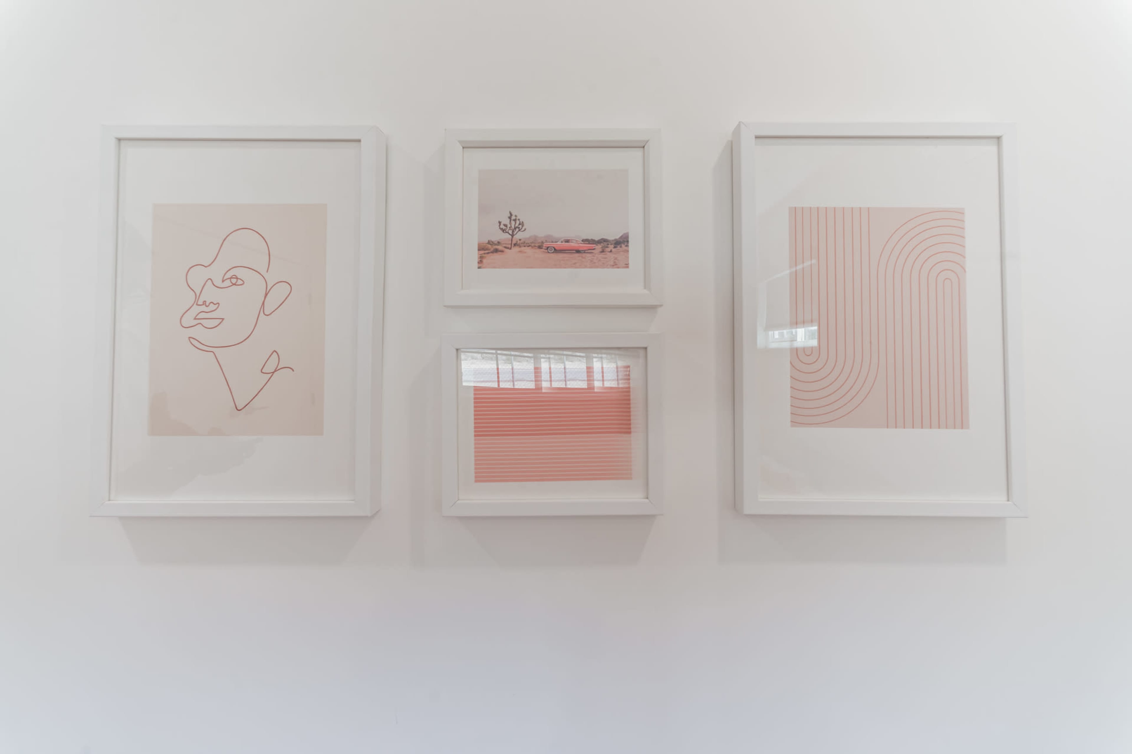 Four framed artworks are displayed on a white wall, featuring minimalist line drawings and abstract patterns in soft pink tones.