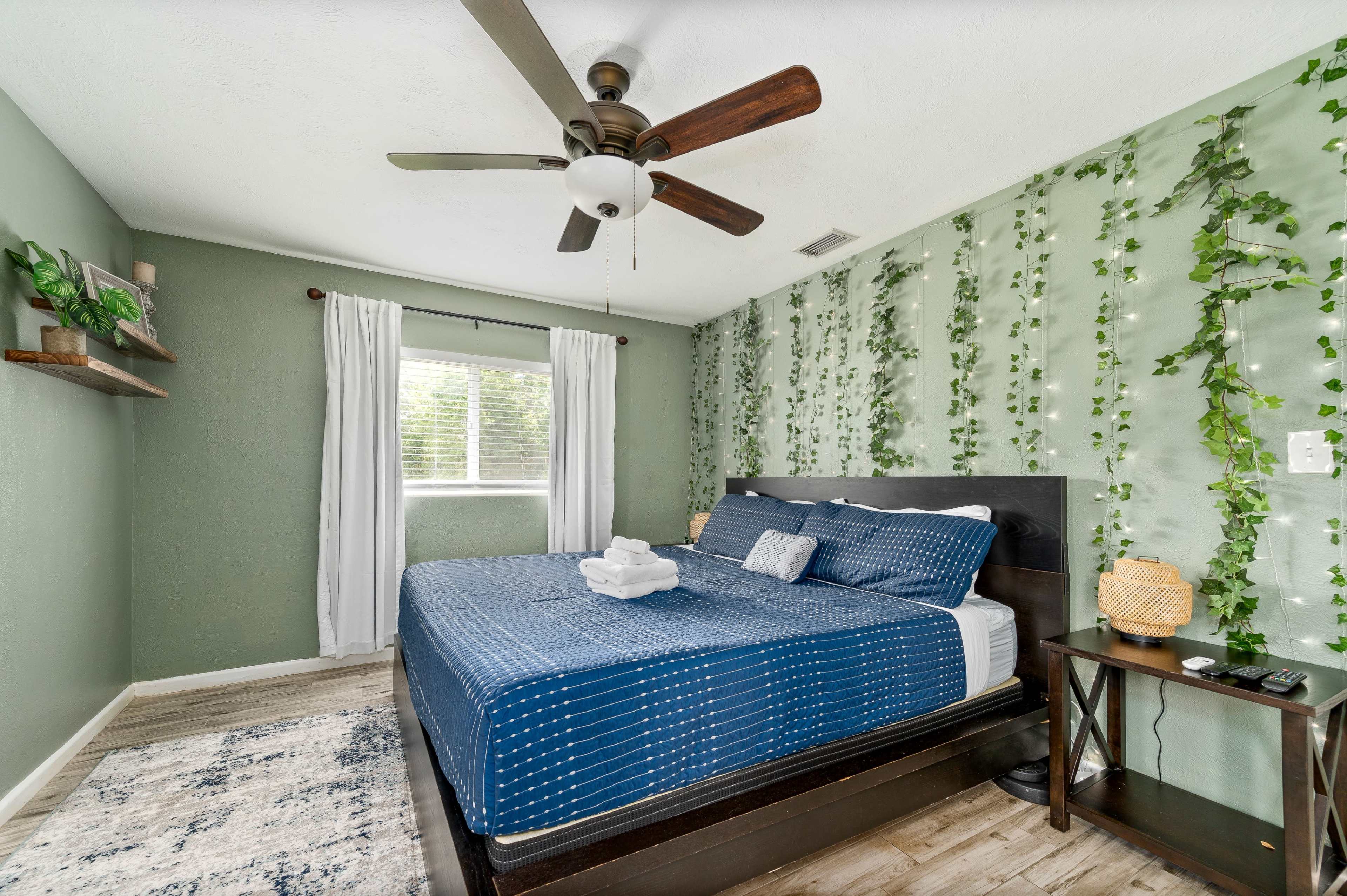 A bedroom features a large bed with a blue comforter, surrounded by green walls adorned with leafy decor.