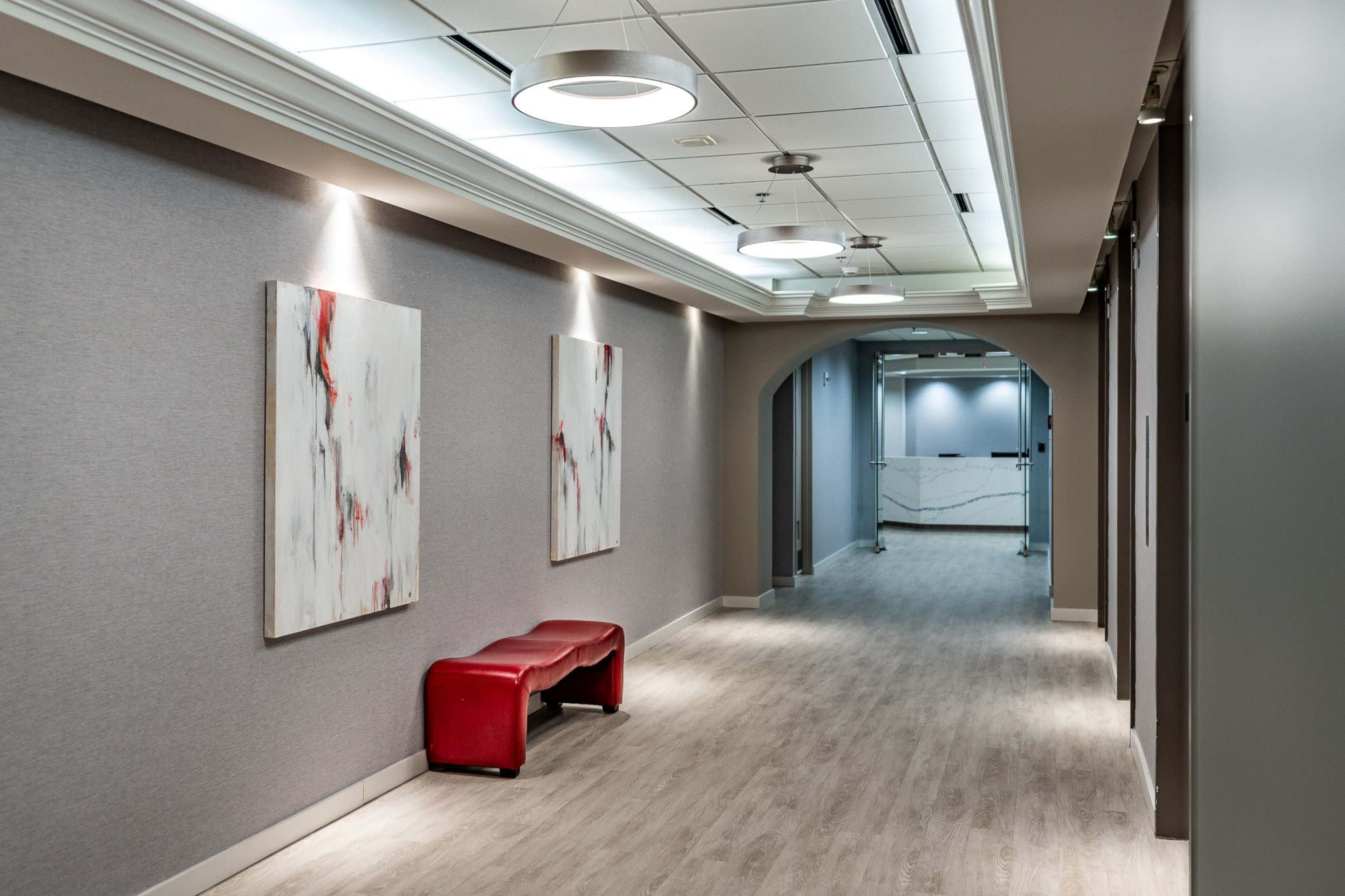 The image shows a long hallway with gray walls, a red bench, and two abstract paintings hanging on the wall.