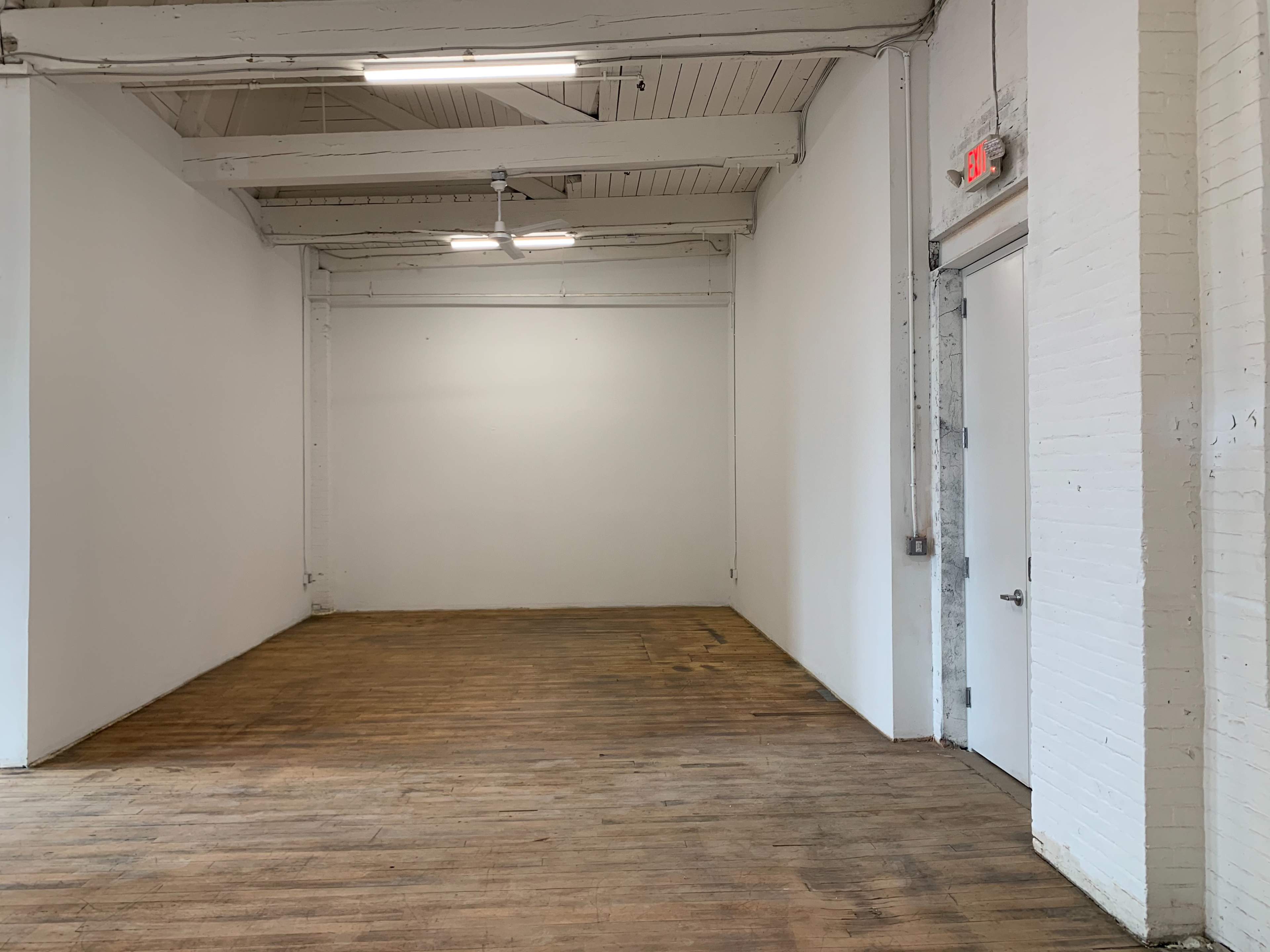 A sparsely furnished, empty room with wooden floors and white walls.