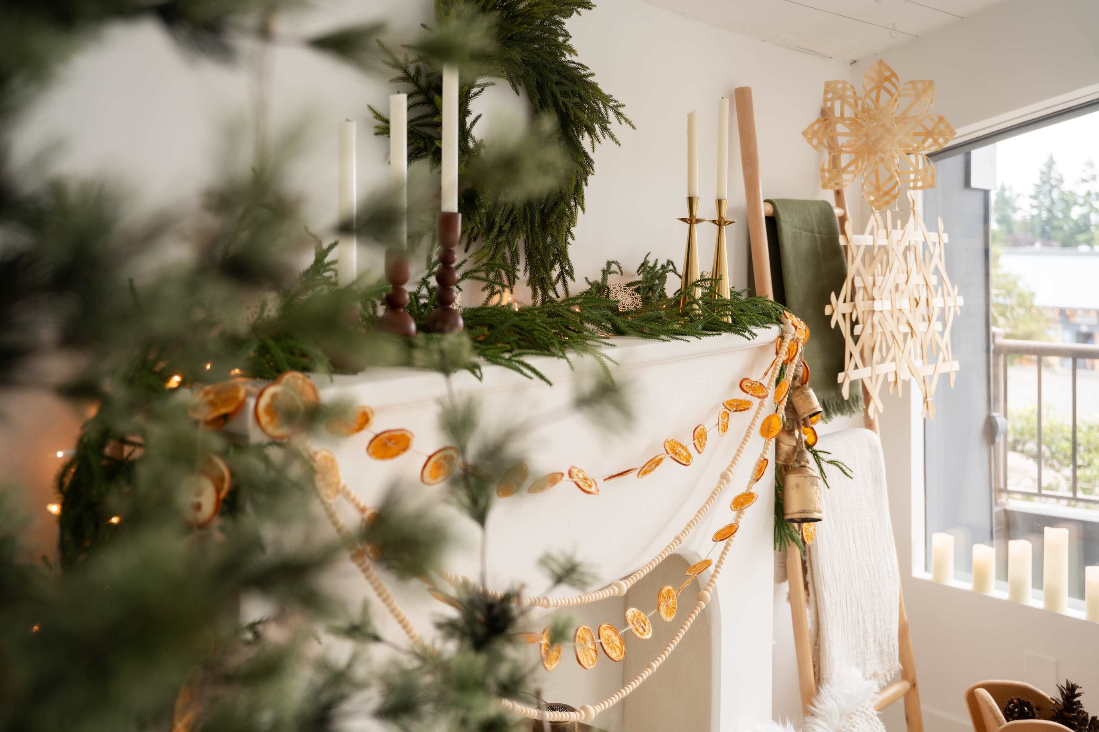 A decorated mantel features green garlands, candles, and orange slice ornaments, alongside winter-themed decor items.