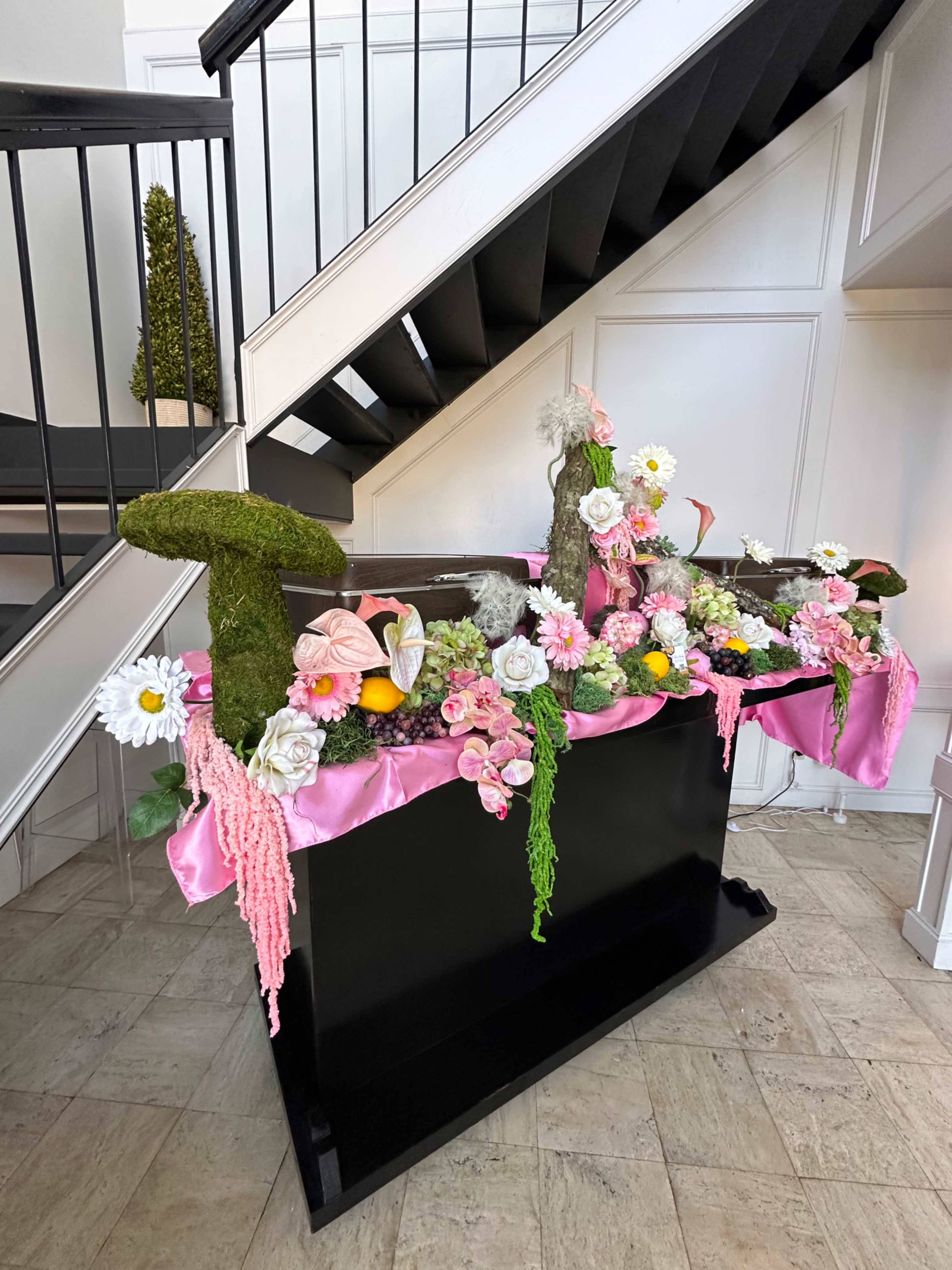 A decorative display featuring bright pink fabric, faux flowers, and mossy letters is positioned at the bottom of a staircase.