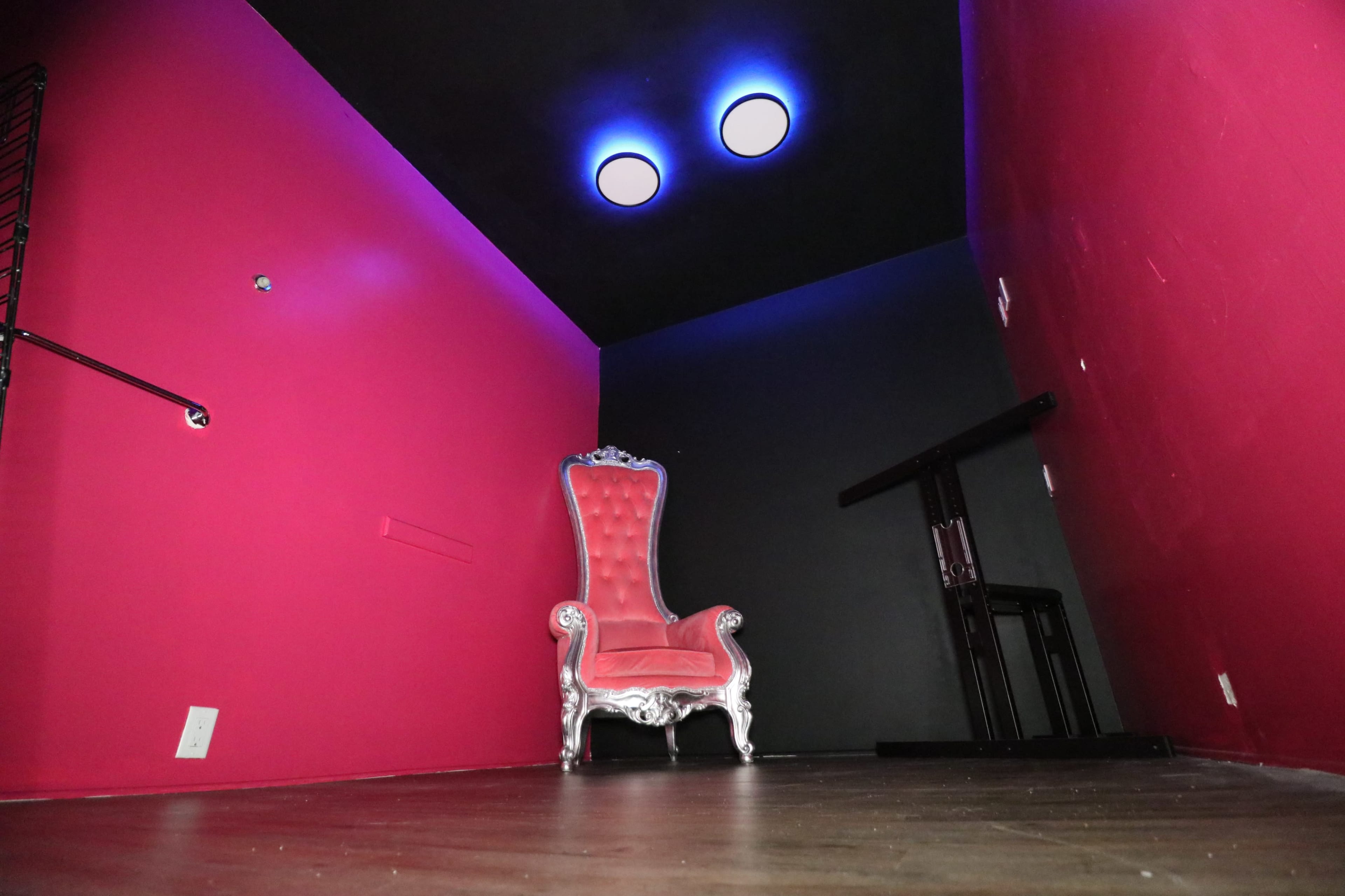 The image shows a corner of a room with a pink wall, a black wall, a silver ornate chair, and two round lights on the ceiling.