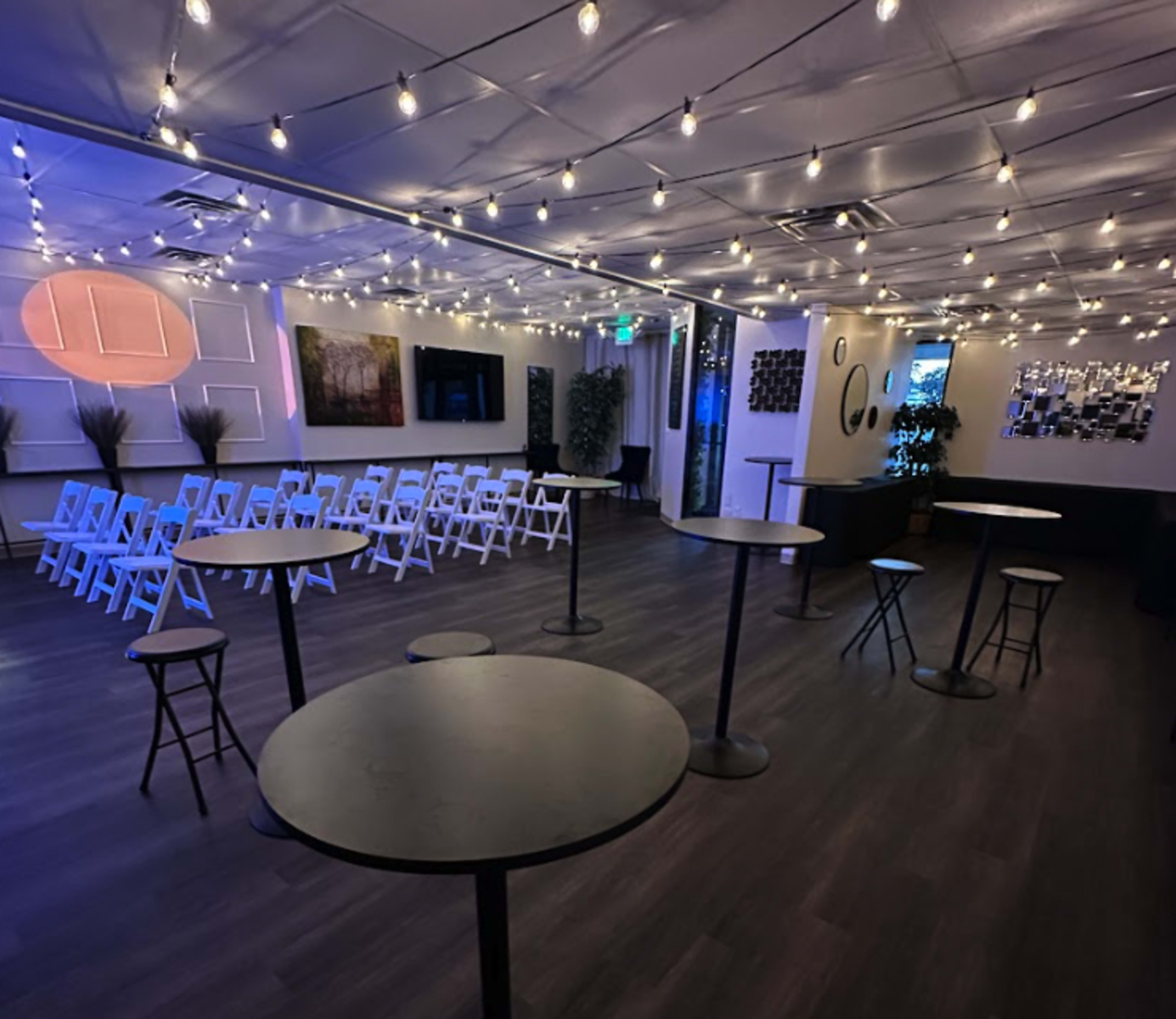 The image shows an indoor event space arranged with chairs, tables, and decorative lighting.