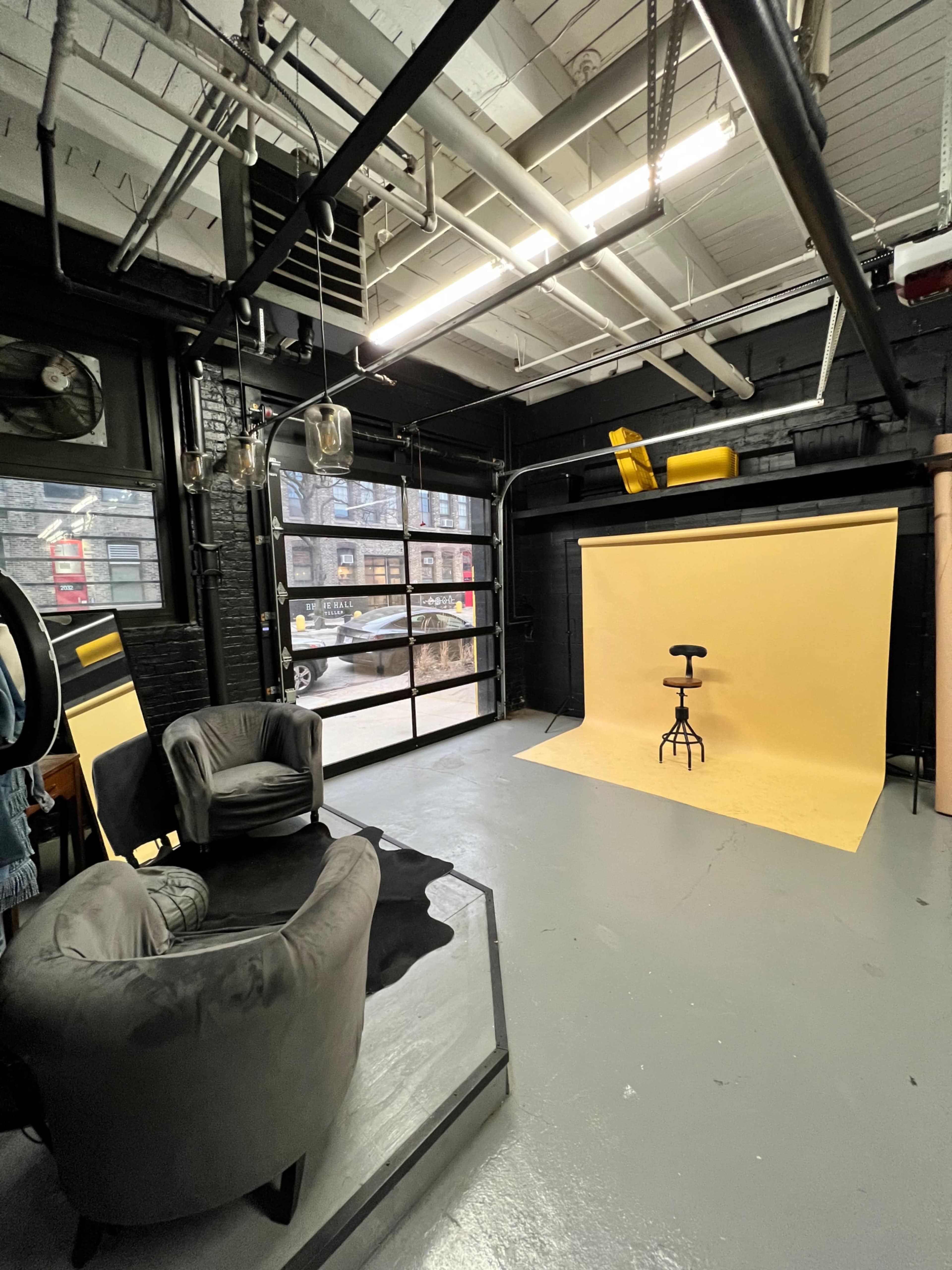 A photography studio featuring a yellow backdrop, a stool, and seating arranged in a corner.