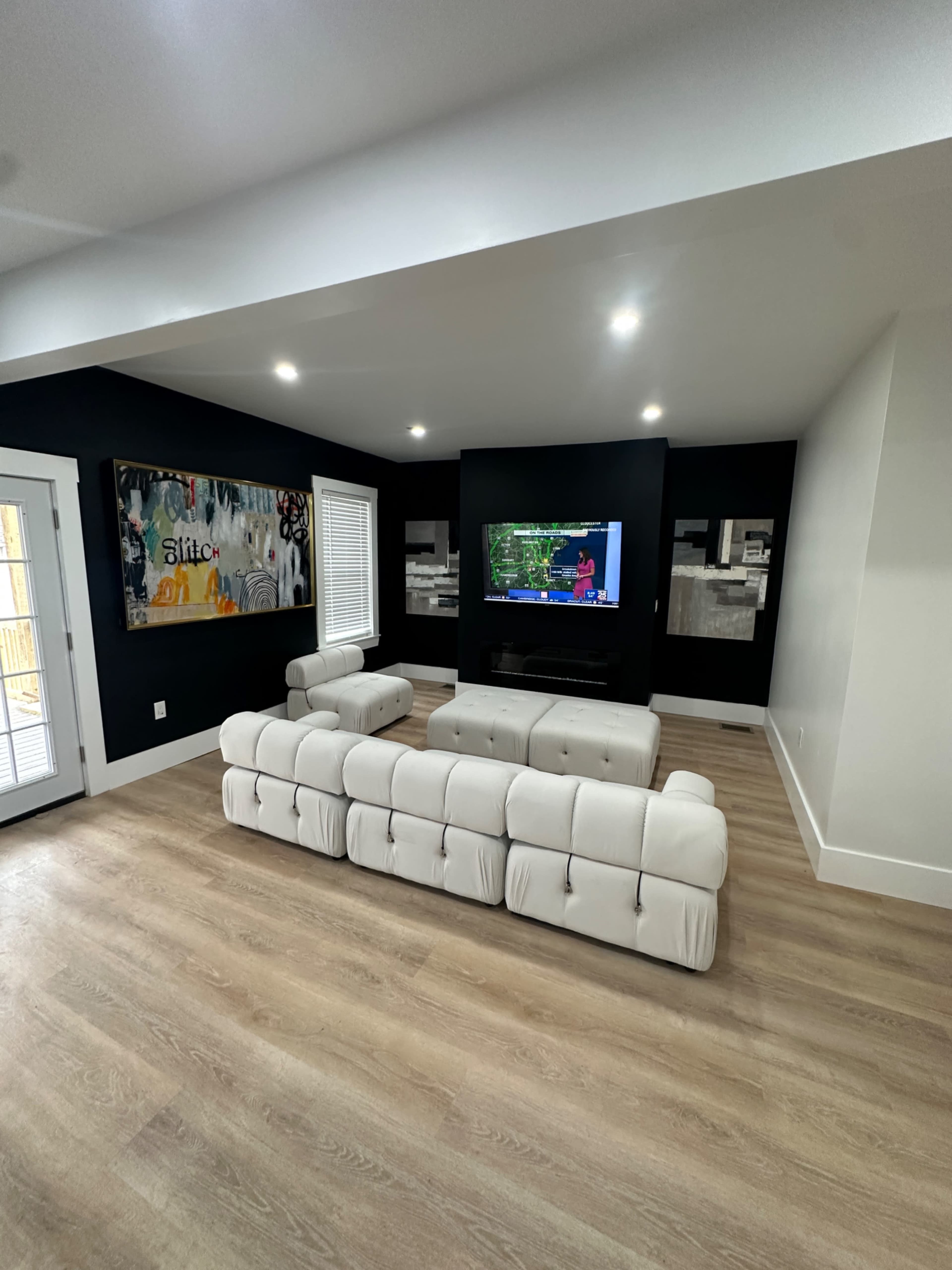A modern living room with a light-colored tufted sofa facing a wall-mounted television and black accent walls.
