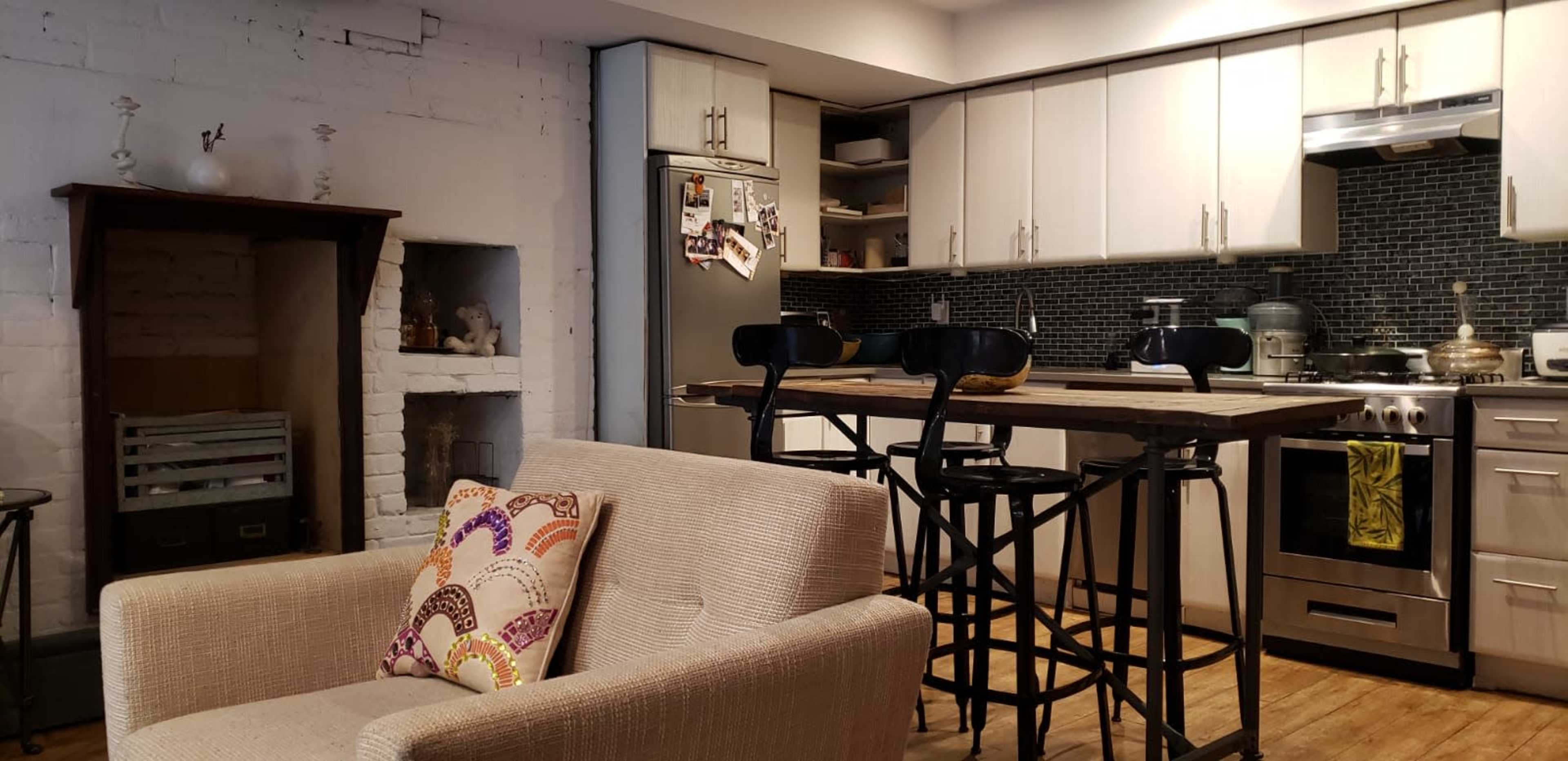 A modern kitchen with stainless steel appliances, a wooden dining table with high chairs, and a cozy seating area featuring a light-colored couch.
