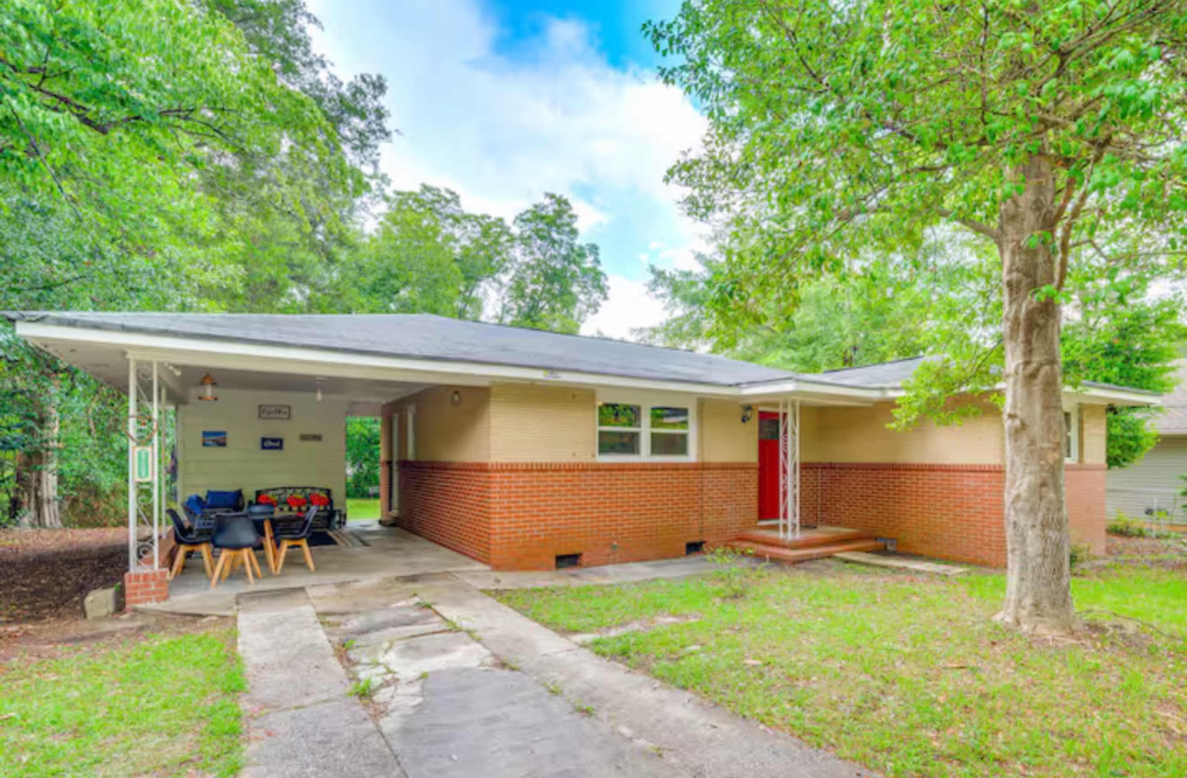 A single-story house with a brick facade and a gray roof is surrounded by trees and has a concrete driveway.