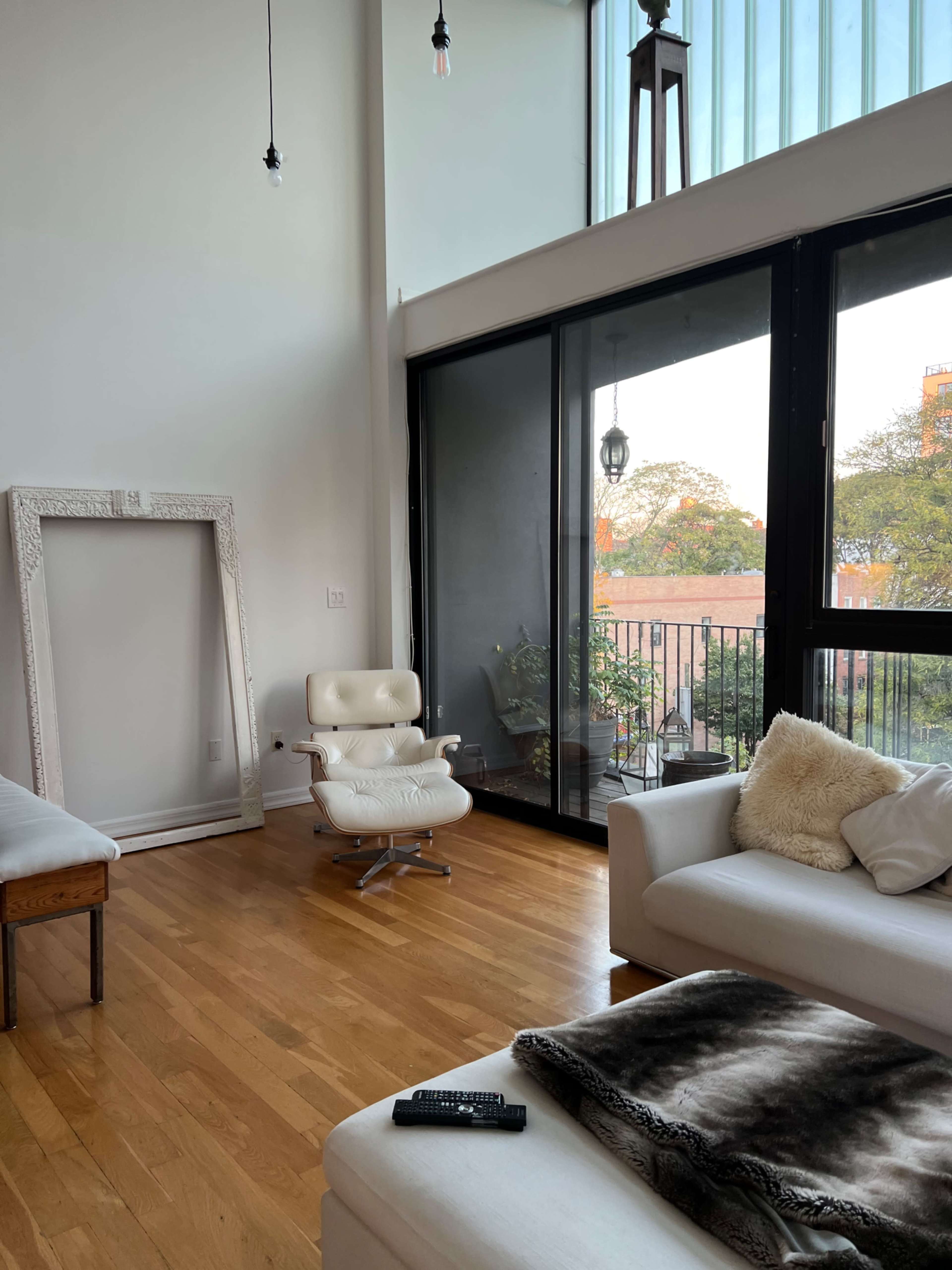 A bright living room with large glass doors leading to a balcony, featuring modern furniture including a white chair and a white sofa.