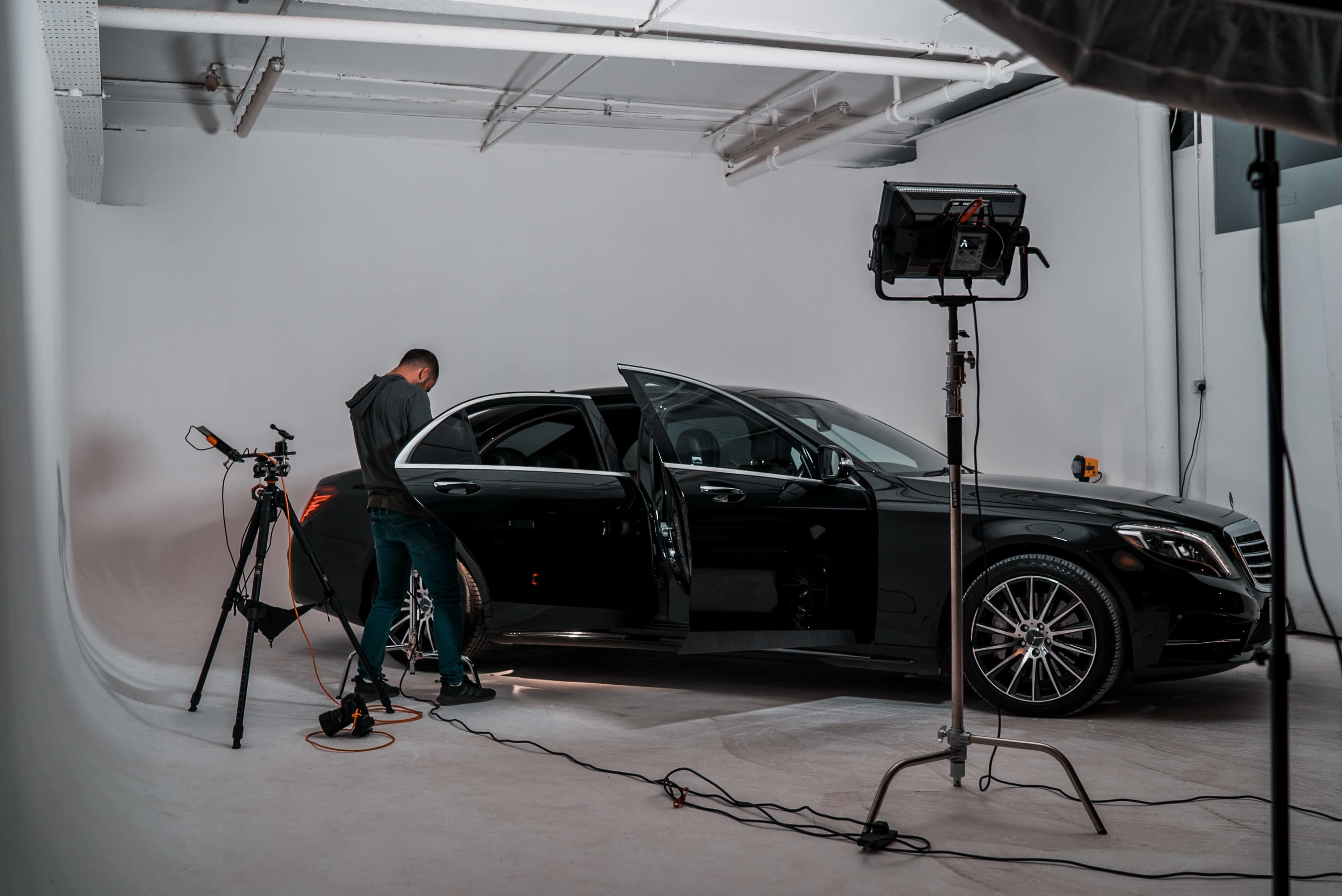 A photographer sets up equipment next to a black luxury car in a well-lit studio.