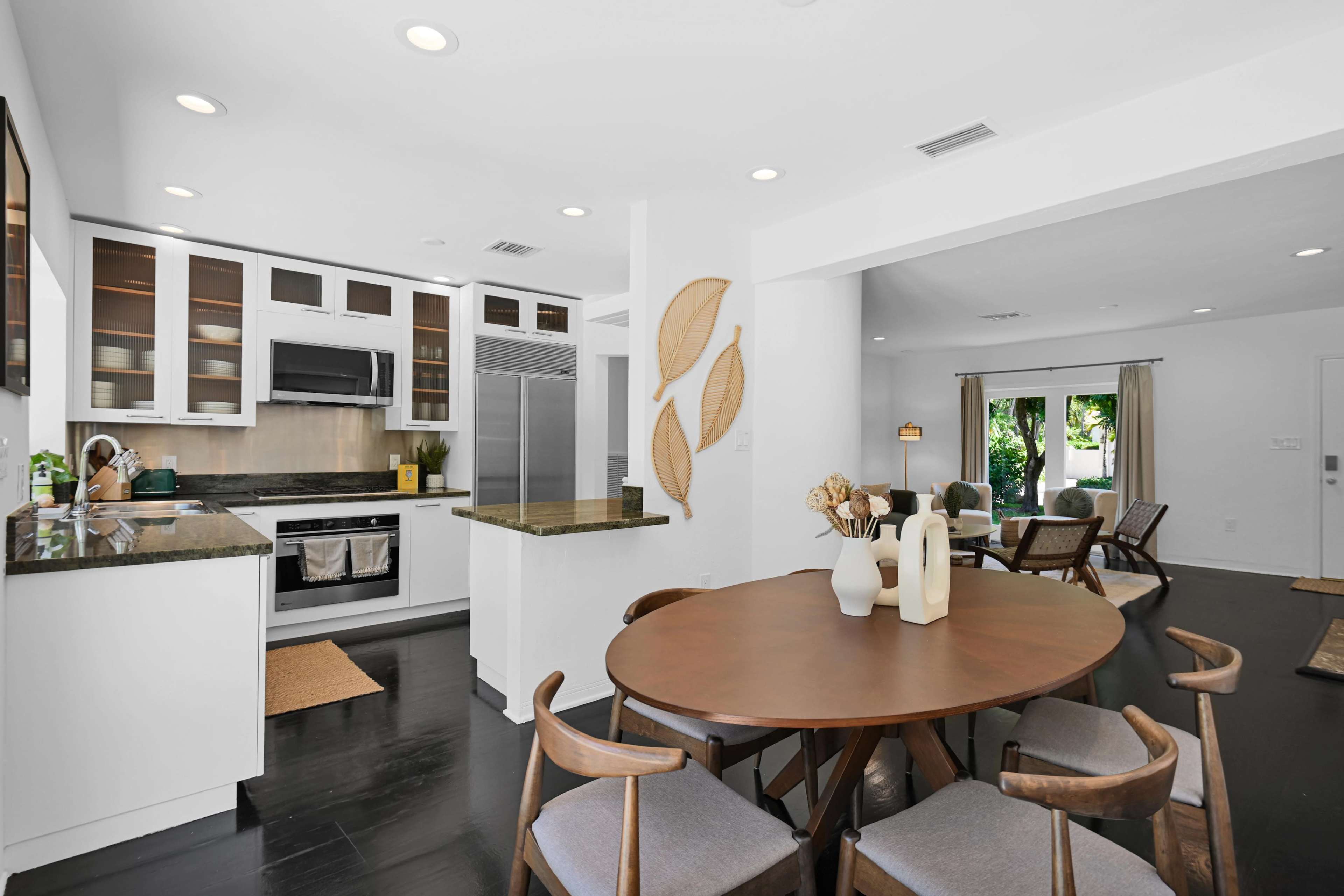 A modern kitchen adjacent to a dining area, featuring white cabinetry, stainless steel appliances, and a round wooden table with chairs.