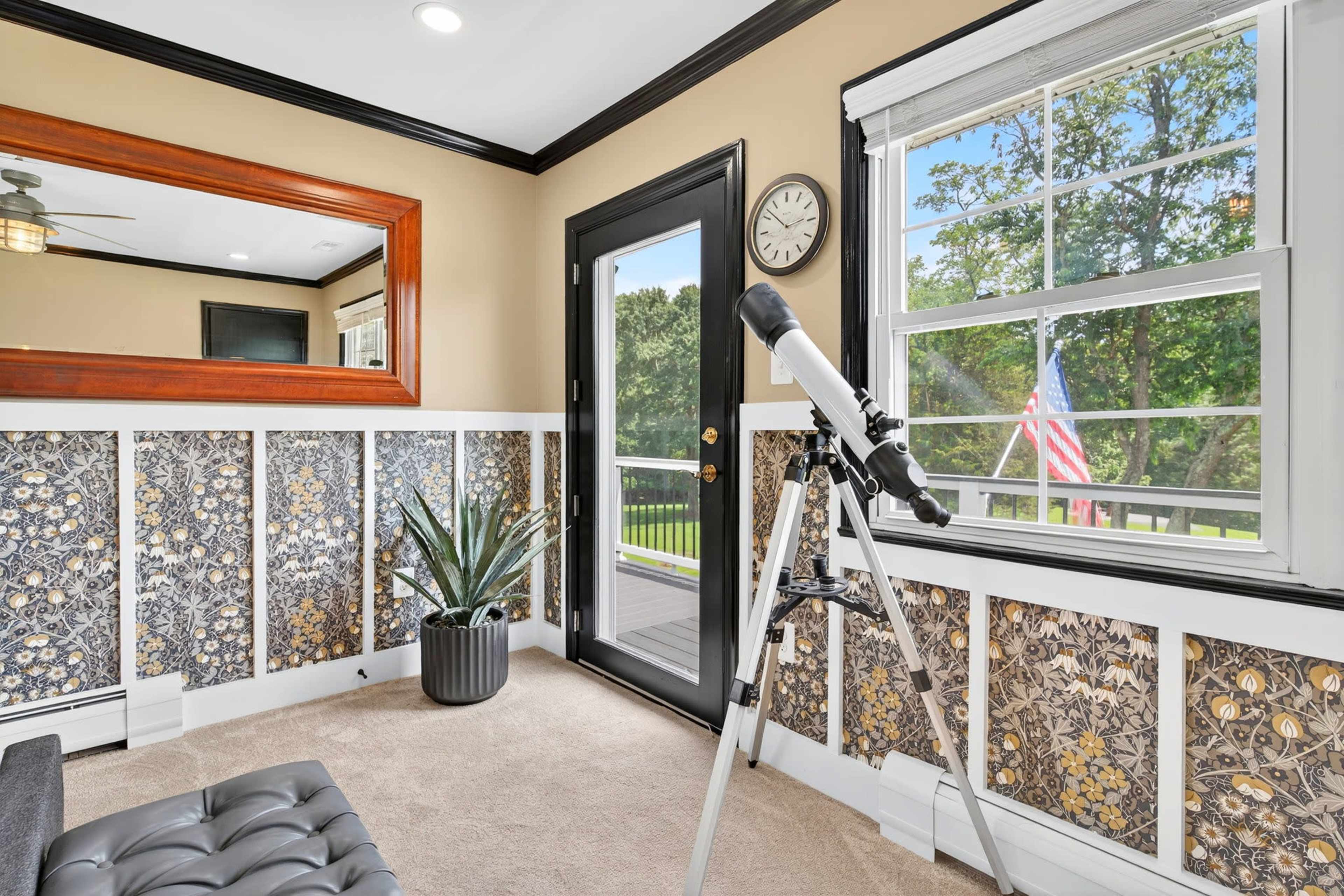 A small room features a telescope positioned near a window, with decorative wallpaper and a door leading outside.