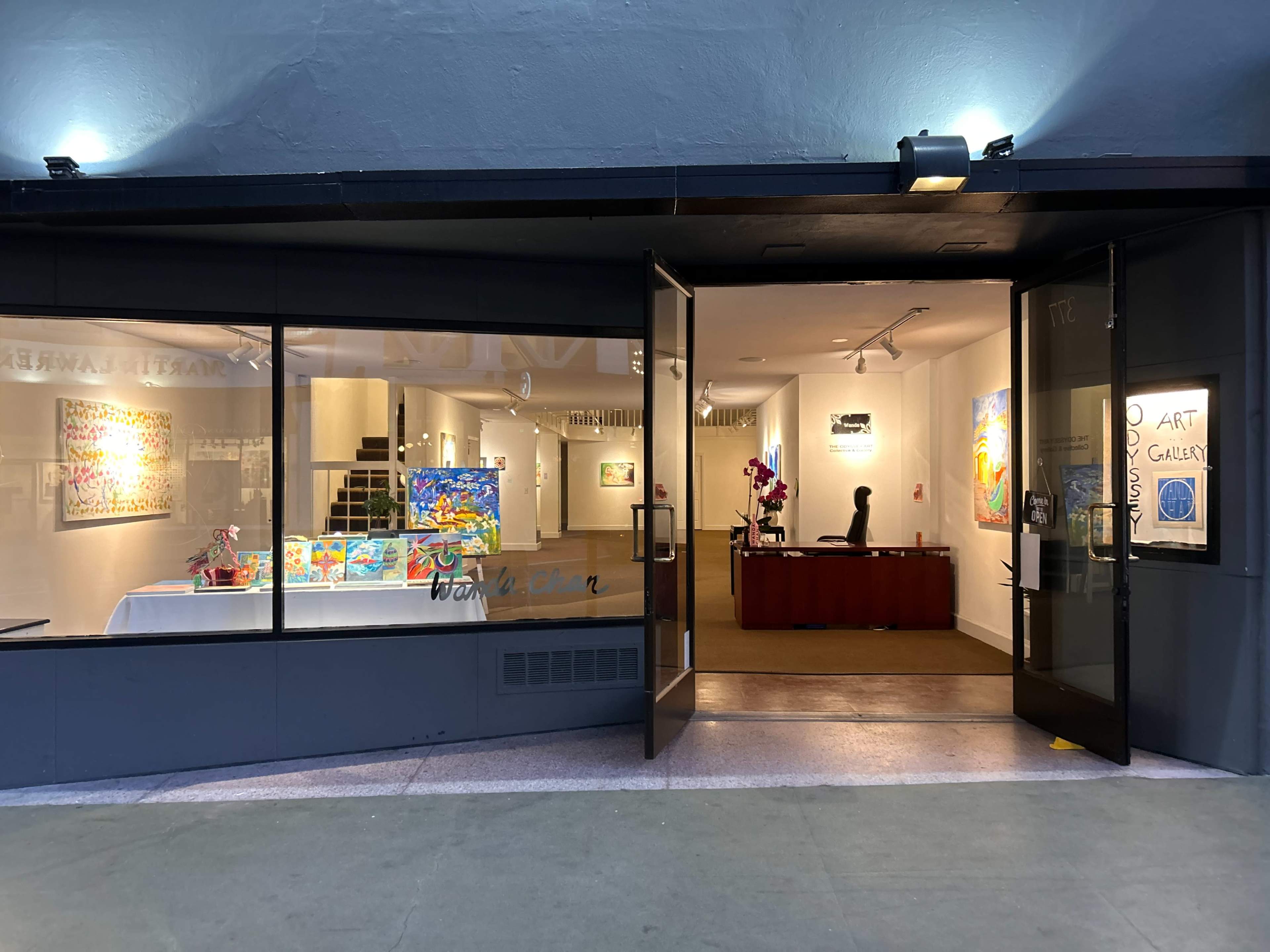 The image shows the entrance of an art gallery with large glass windows and bright artwork displayed inside.
