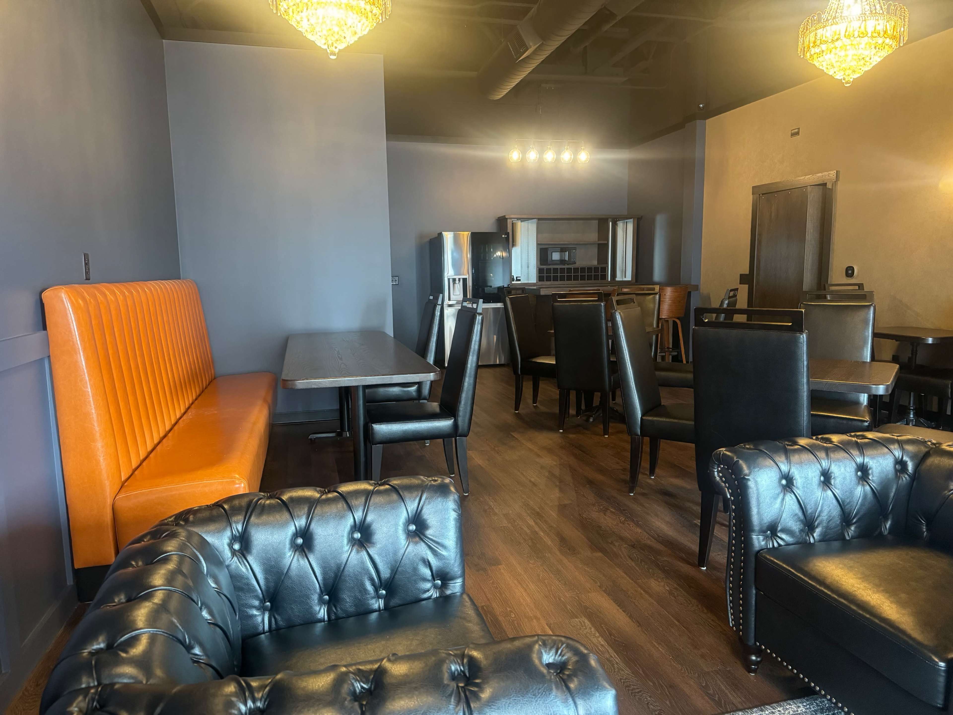 The image shows a modern dining area featuring black leather seating, an orange booth, and a range of tables and chairs under decorative lighting.