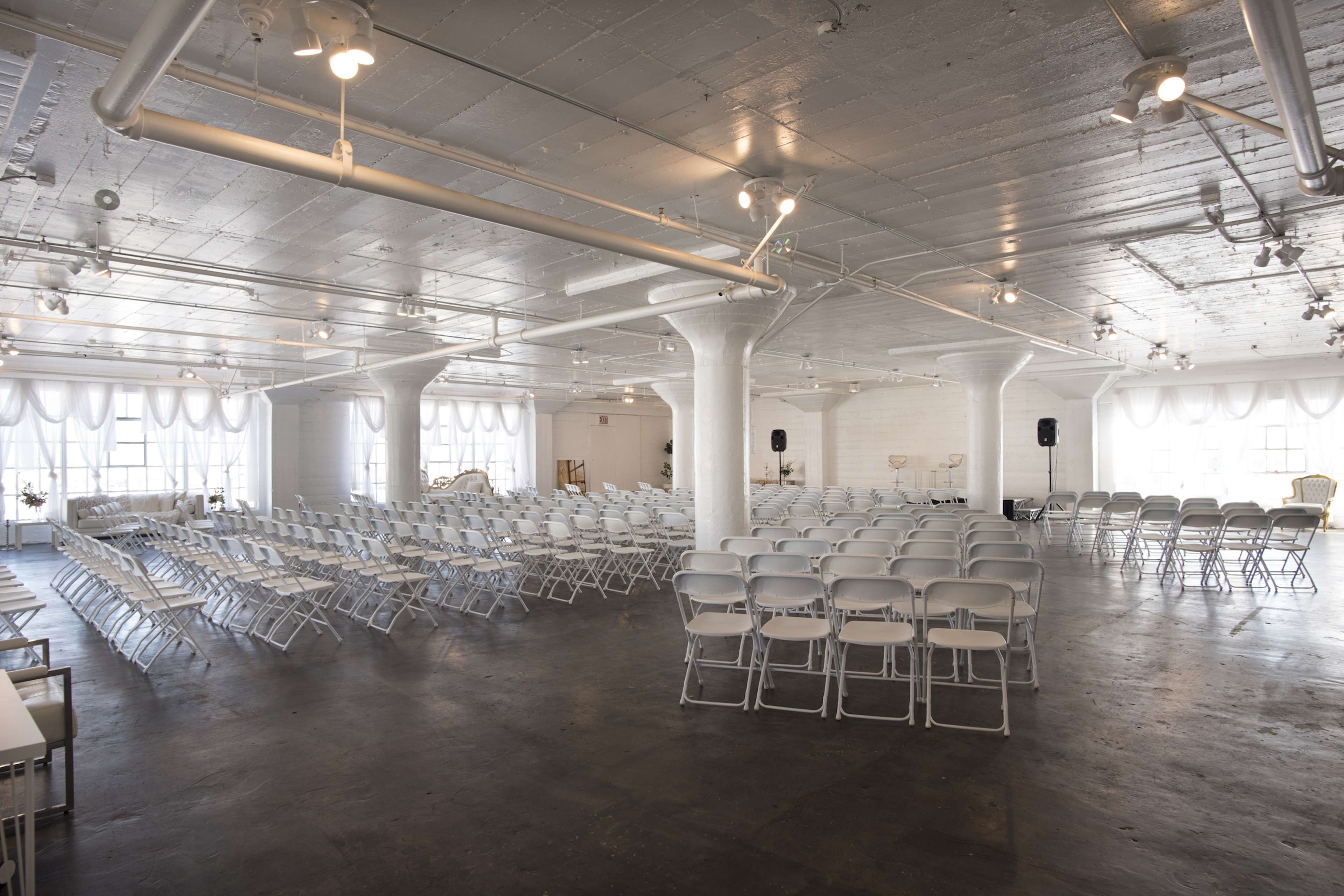 A spacious, well-lit event room arranged with rows of white folding chairs facing a stage area.