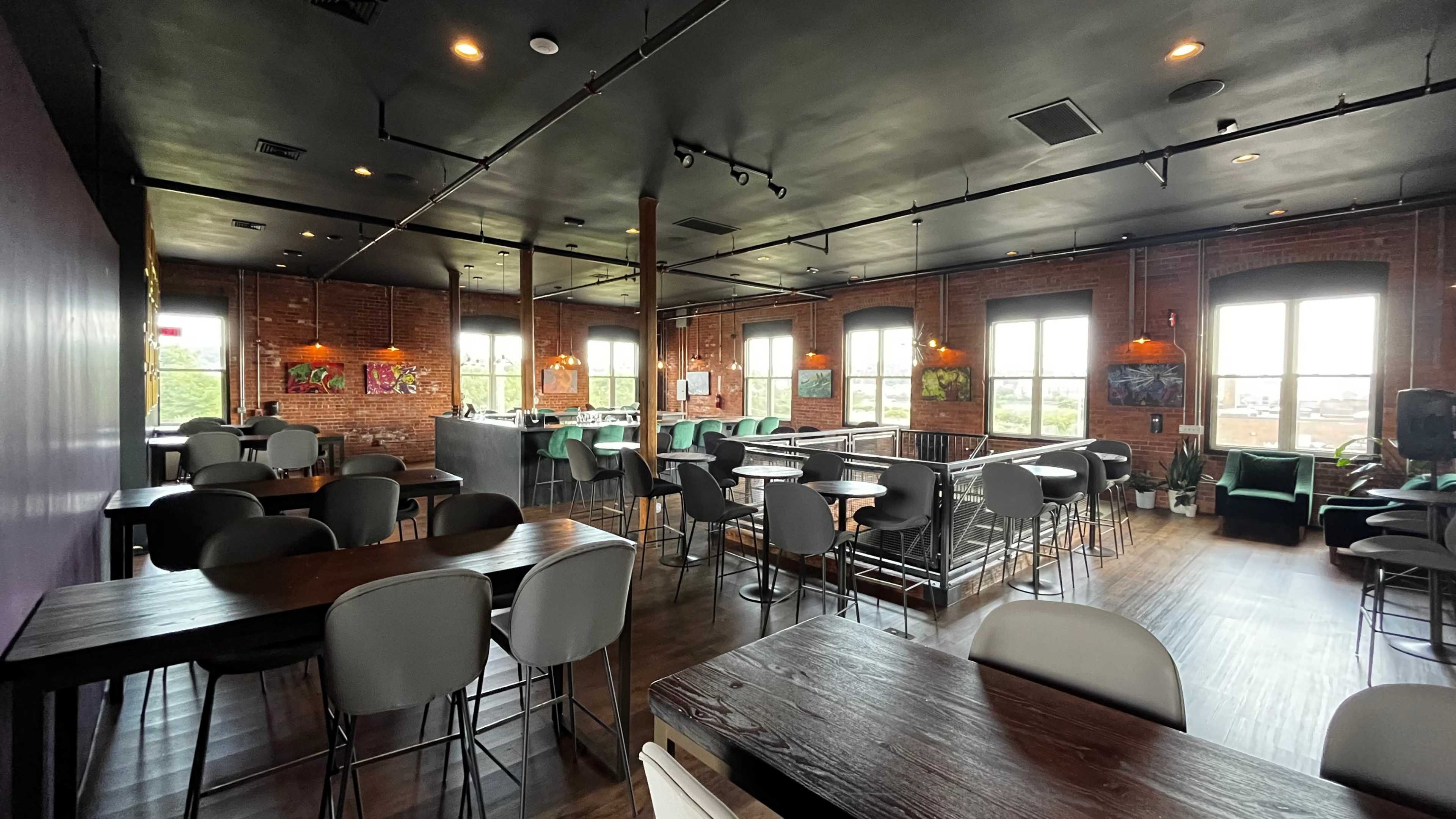 A modern, open dining area with empty tables and chairs, large windows, and colorful artwork on the walls.
