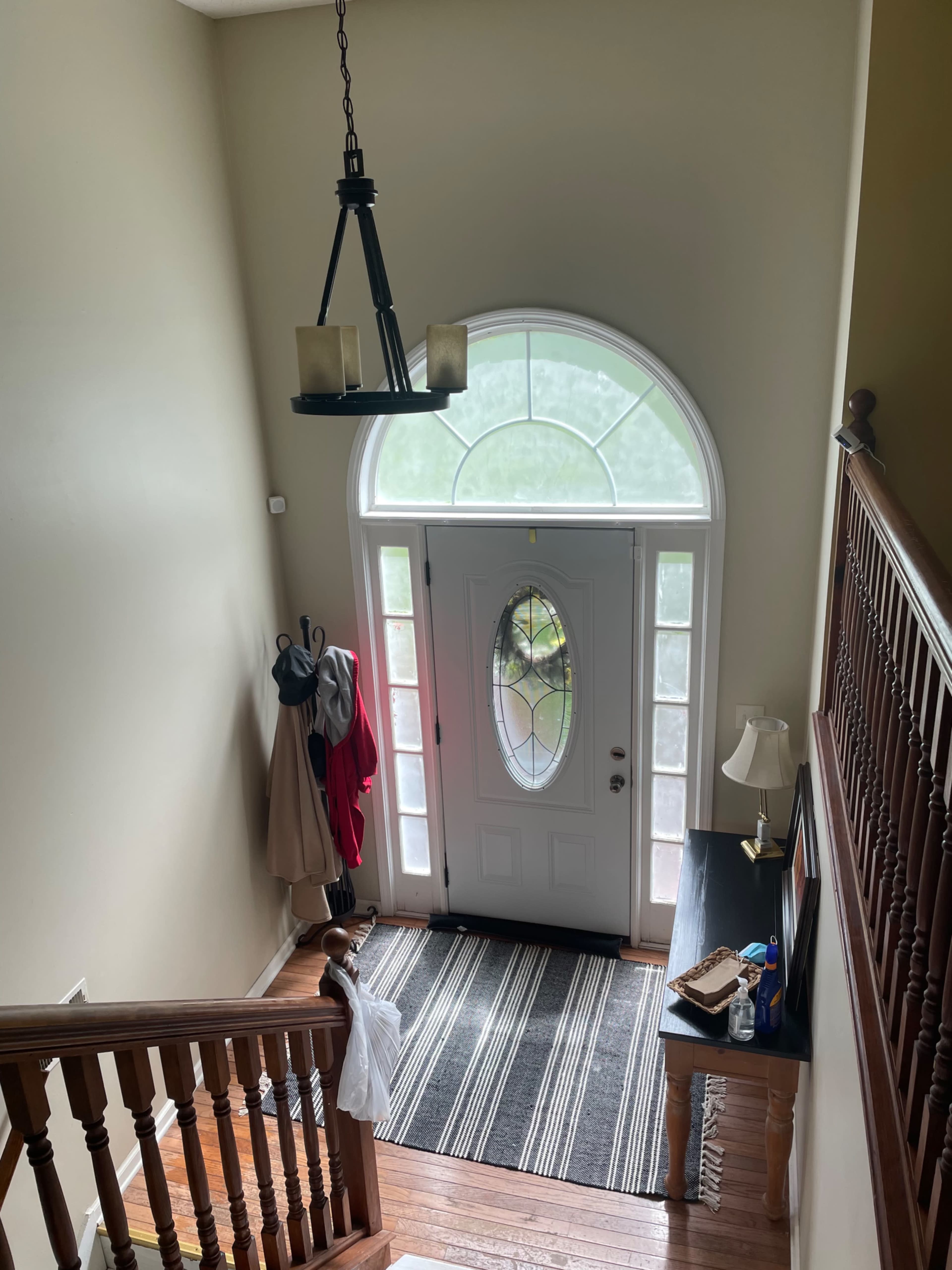 The entryway of a home with a chandelier, a door with a large window, a staircase, a coat rack, and a small table.